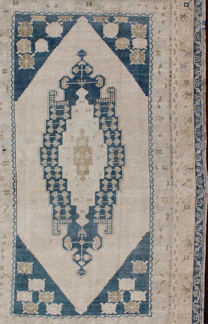 Medallion design Oushak rug from Turkey in cream, tan, and blue tones, rug TU-MTU-4923, country of origin / type: Turkey / Oushak, circa 1940

This vintage Turkish Oushak rug features a unique medallion design. The multi-banded border frames the