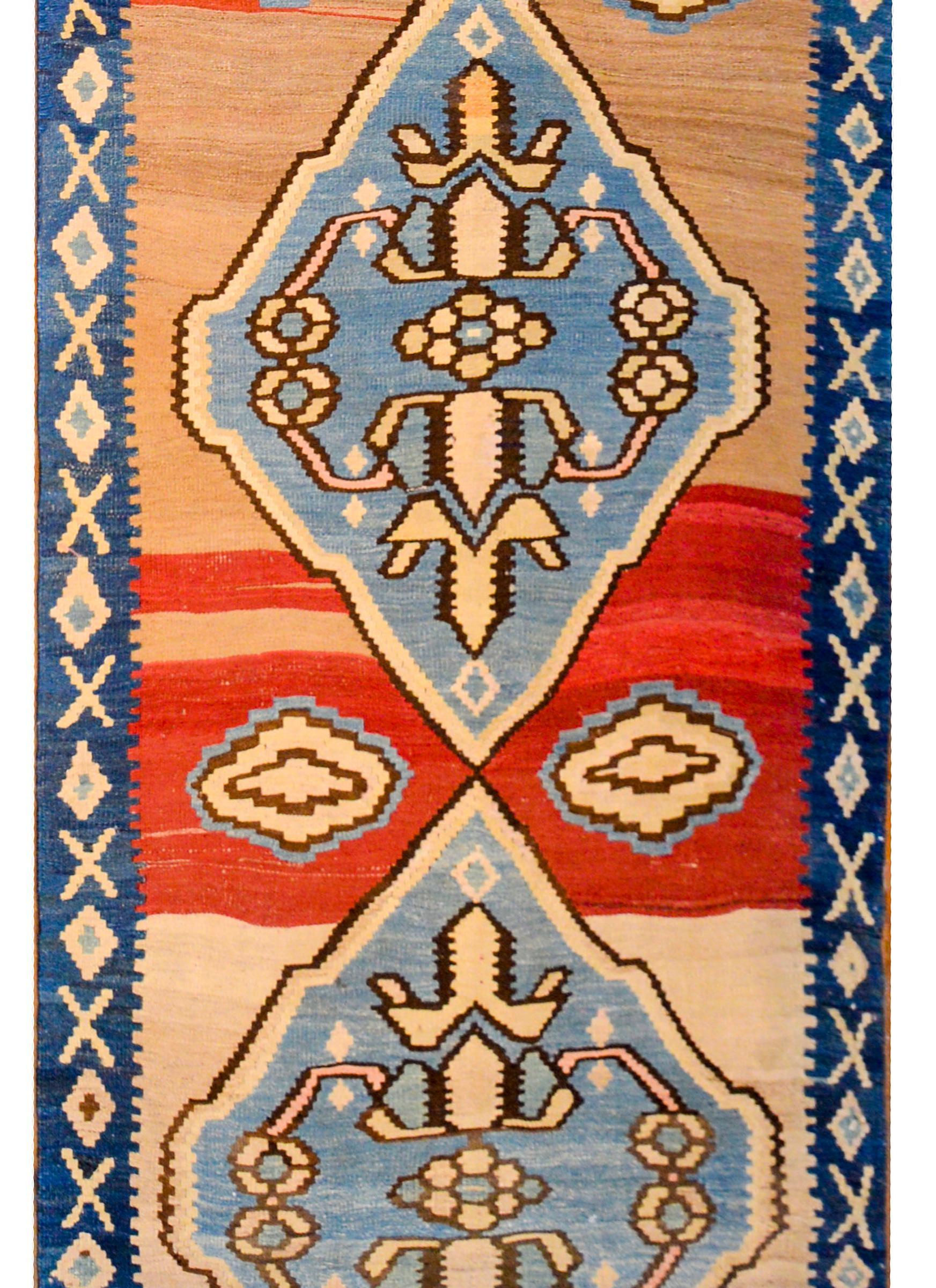 A bold early 20th century Azerbaijani Azari KIlim runner of considerable length with four large indigo diamond medallions with gold floral patterns on an abrash crimson and orange background. The border is simple with a petite geometric pattern in