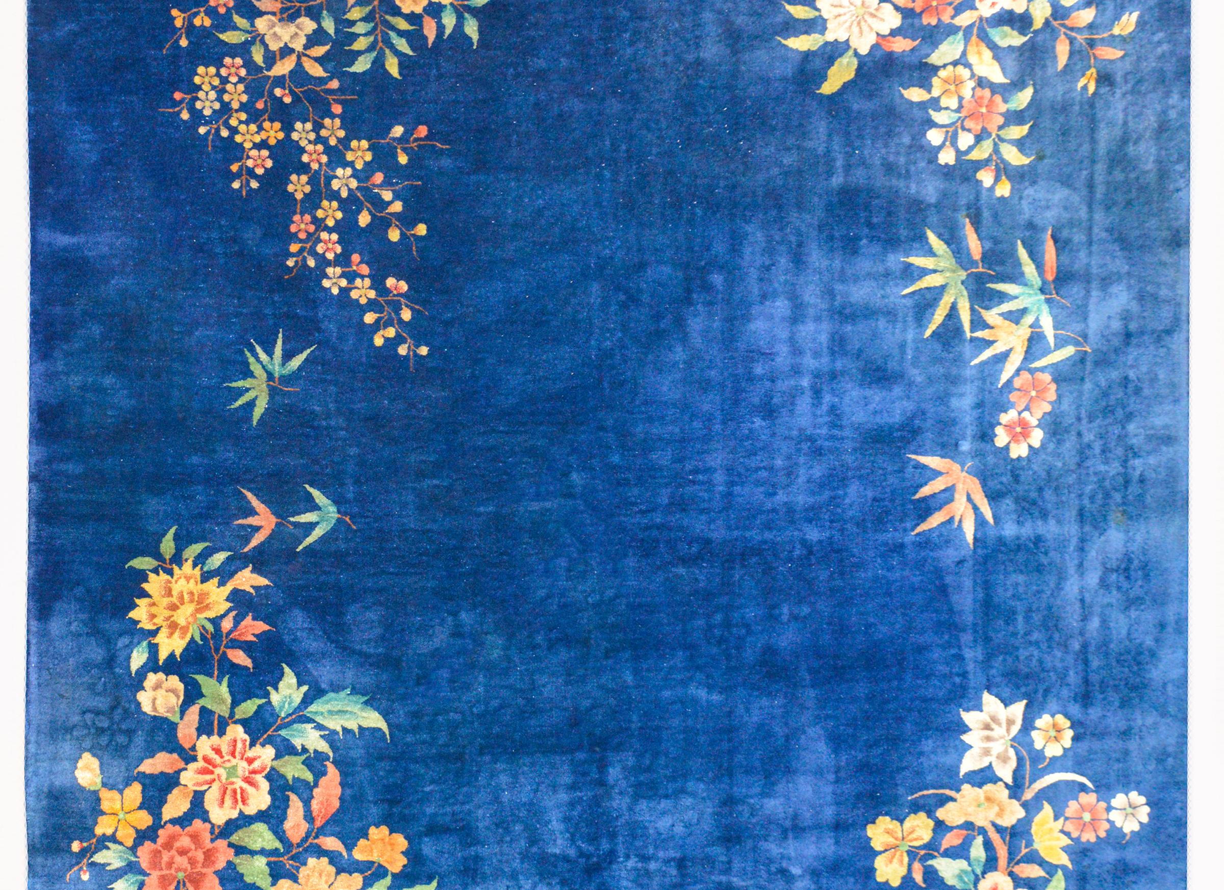 A bold early 20th century Chinese Art Deco rug with a rich indigo field with large multicolored peonies and scrolling leafy branches in each corner.