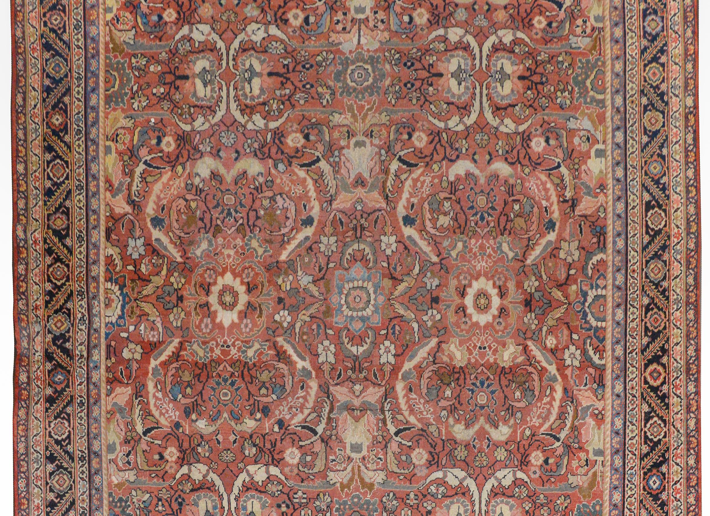 A bold early 20th century Persian Mahal rug with a large-scale mirrored floral and scrolling vine pattern woven in light and dark indigo, cream, pink, and brown colored vegetable dyed wool on a dark crimson background. The border is wonderful with a