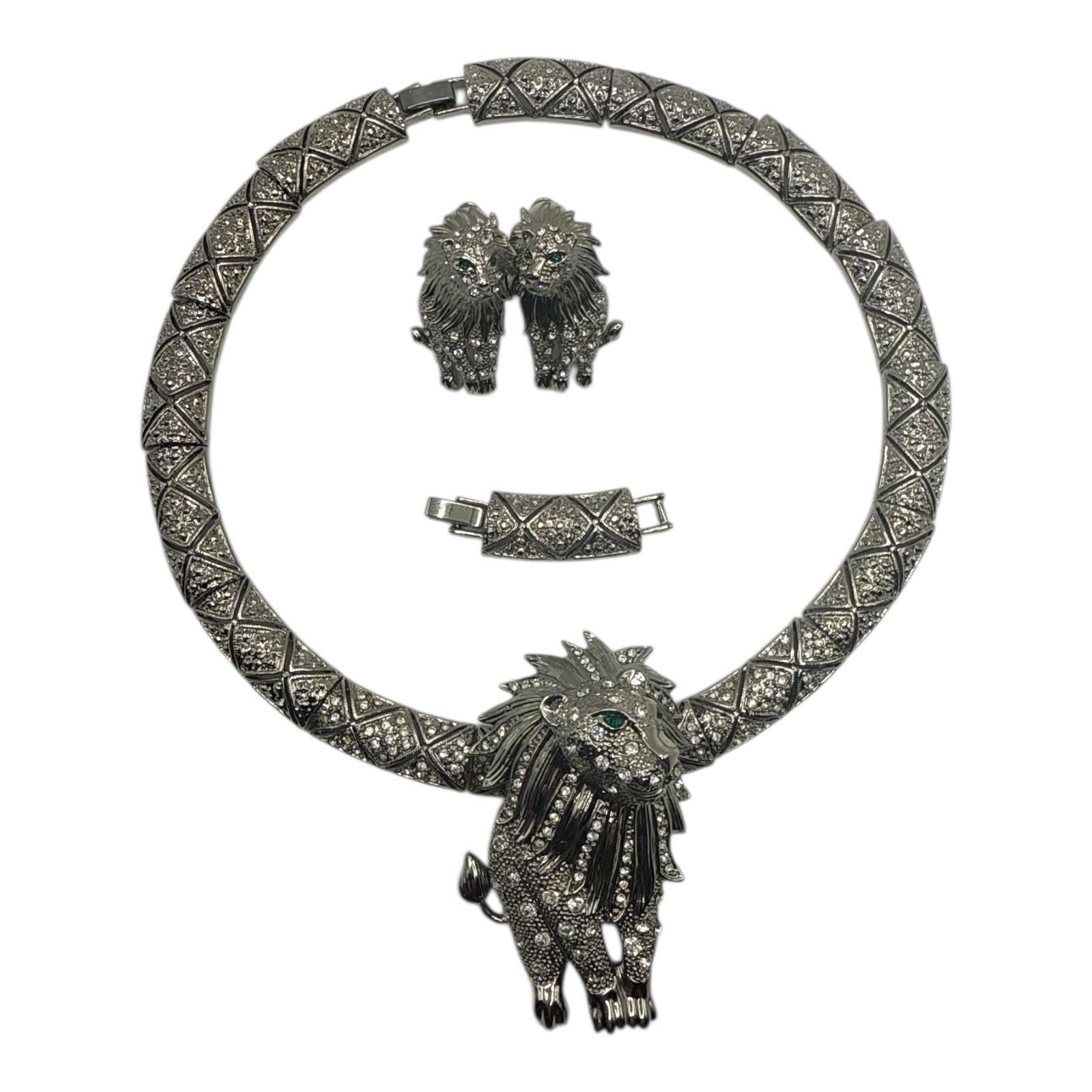 Bold and regal, this vintage-style jewelry set features a striking lion motif encrusted with brilliant clear crystals. The necklace showcases a large sculptural lion pendant with a highly detailed mane, emerald green crystal eyes, and textured body,