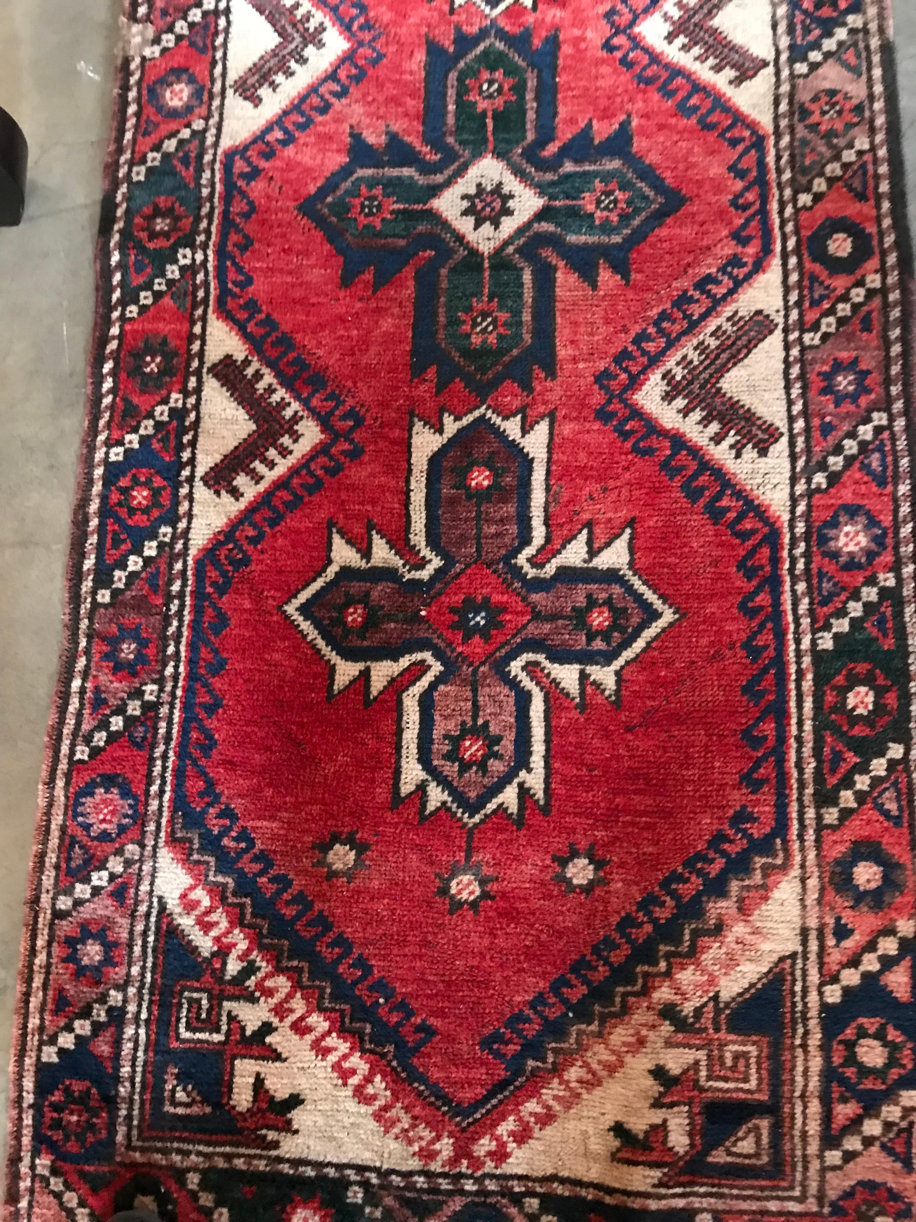 This textured Kilim runner stands out in deep red color with seven medallion crosses alternating in brown and black as well as repeated patterns of diamonds and triangles along the edges. White fringe outlines both ends.
 