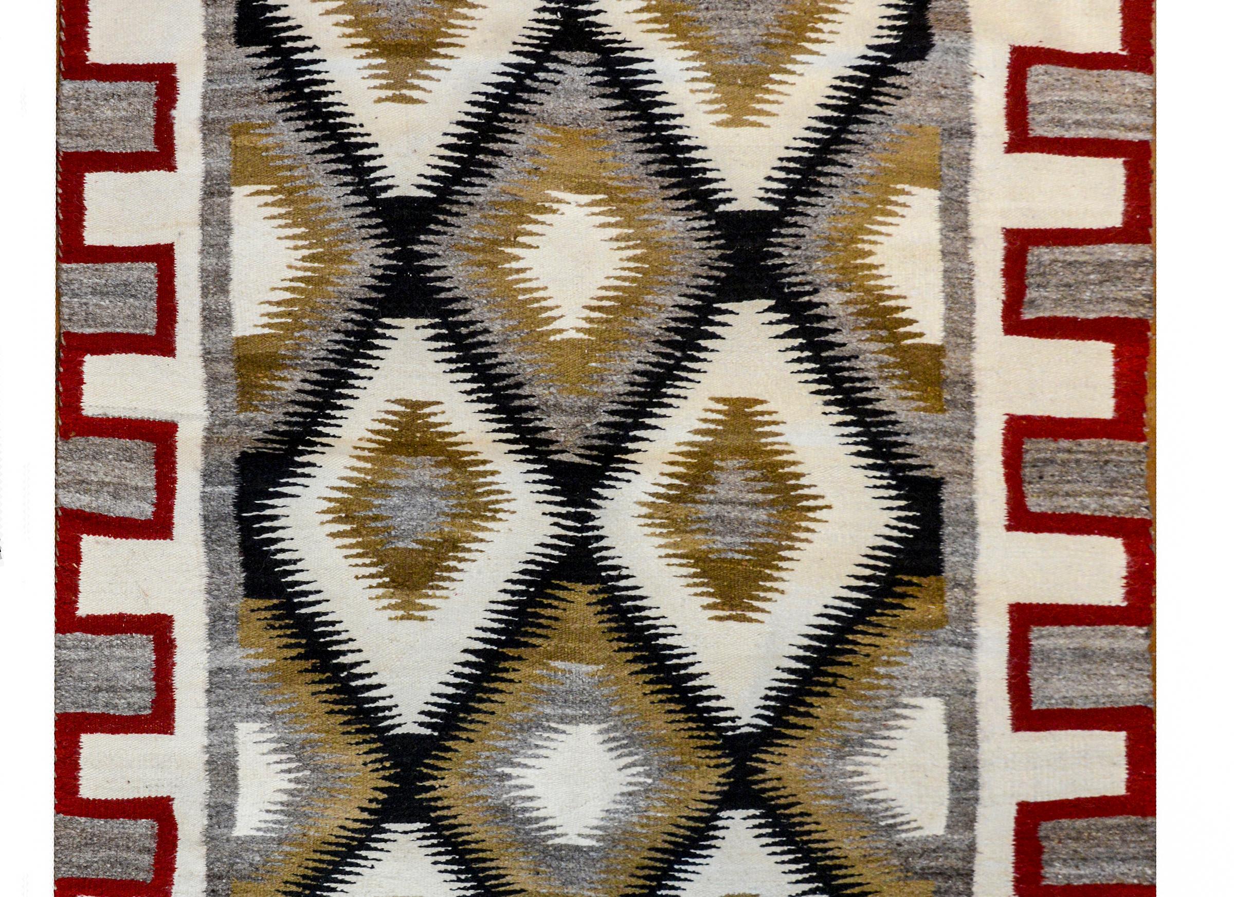 A bold mid-20th century Navajo rug with an all-over diamond pattern woven in black, white, and brown wool surrounded by a wide crimson, white, and gray stepped border.