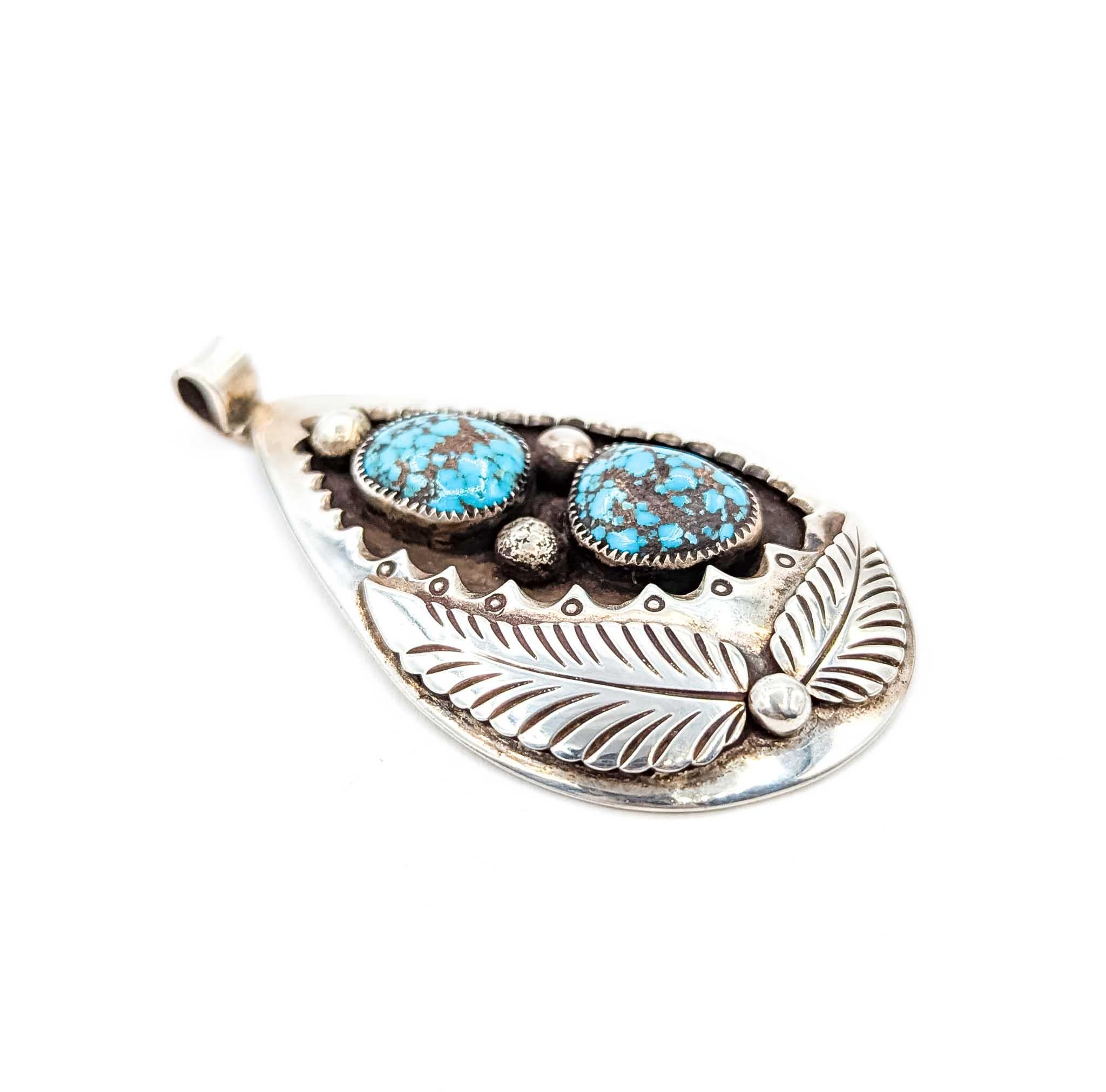 Questo sorprendente ciondolo dei nativi americani è realizzato a mano in argento sterling e presenta due grandi cabochon di turchese con suggestivi motivi a matrice marrone e nera. Le pietre sono incastonate all'interno di una cornice a forma di