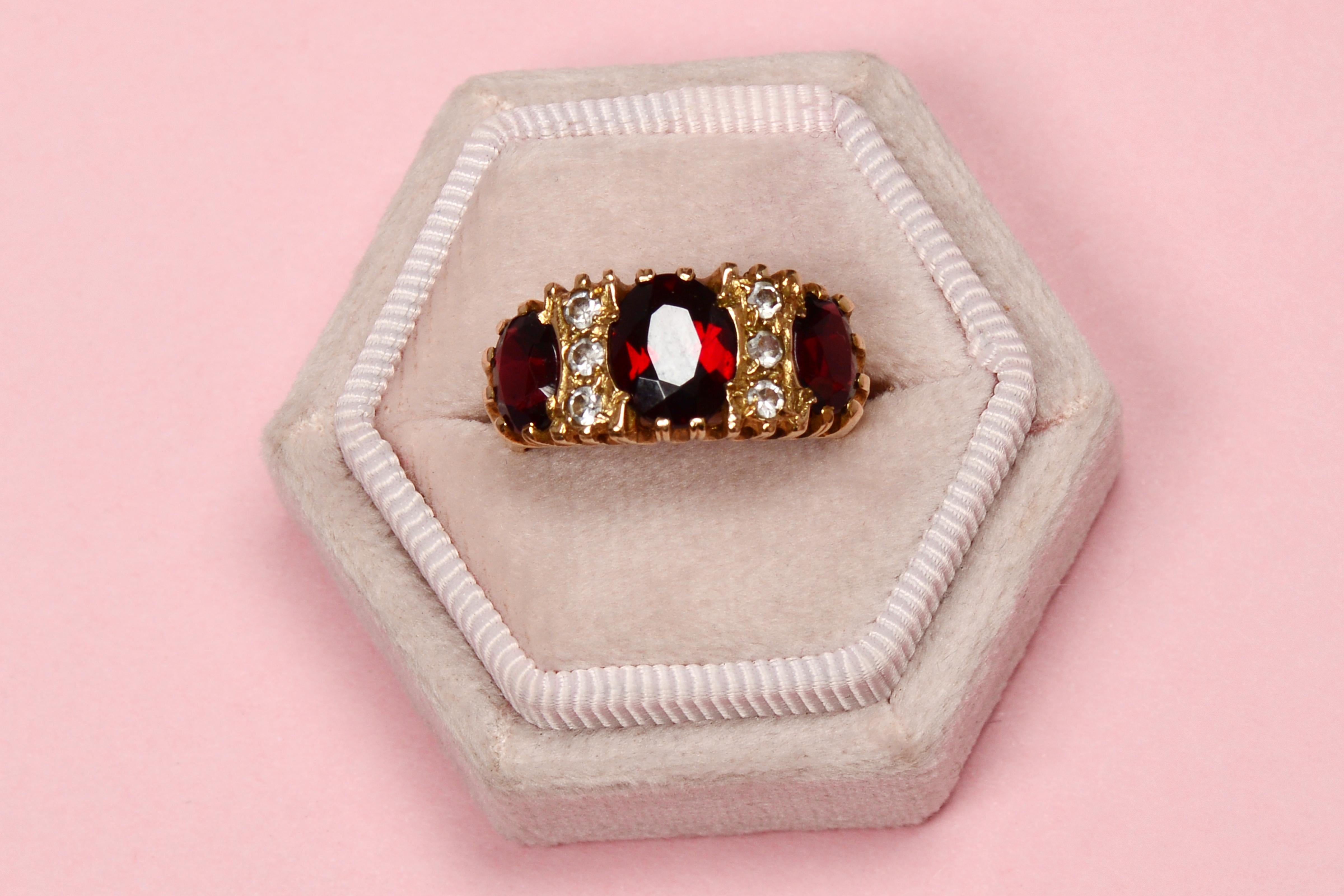 The ring glows a warm burgundy color set with three oval faceted garnets so that you can taste the wine! Between the garnets are rock crystals, six of them that are as bright as diamonds. The ring is 9 kt gold, stronger than 15 Kt. It is English
