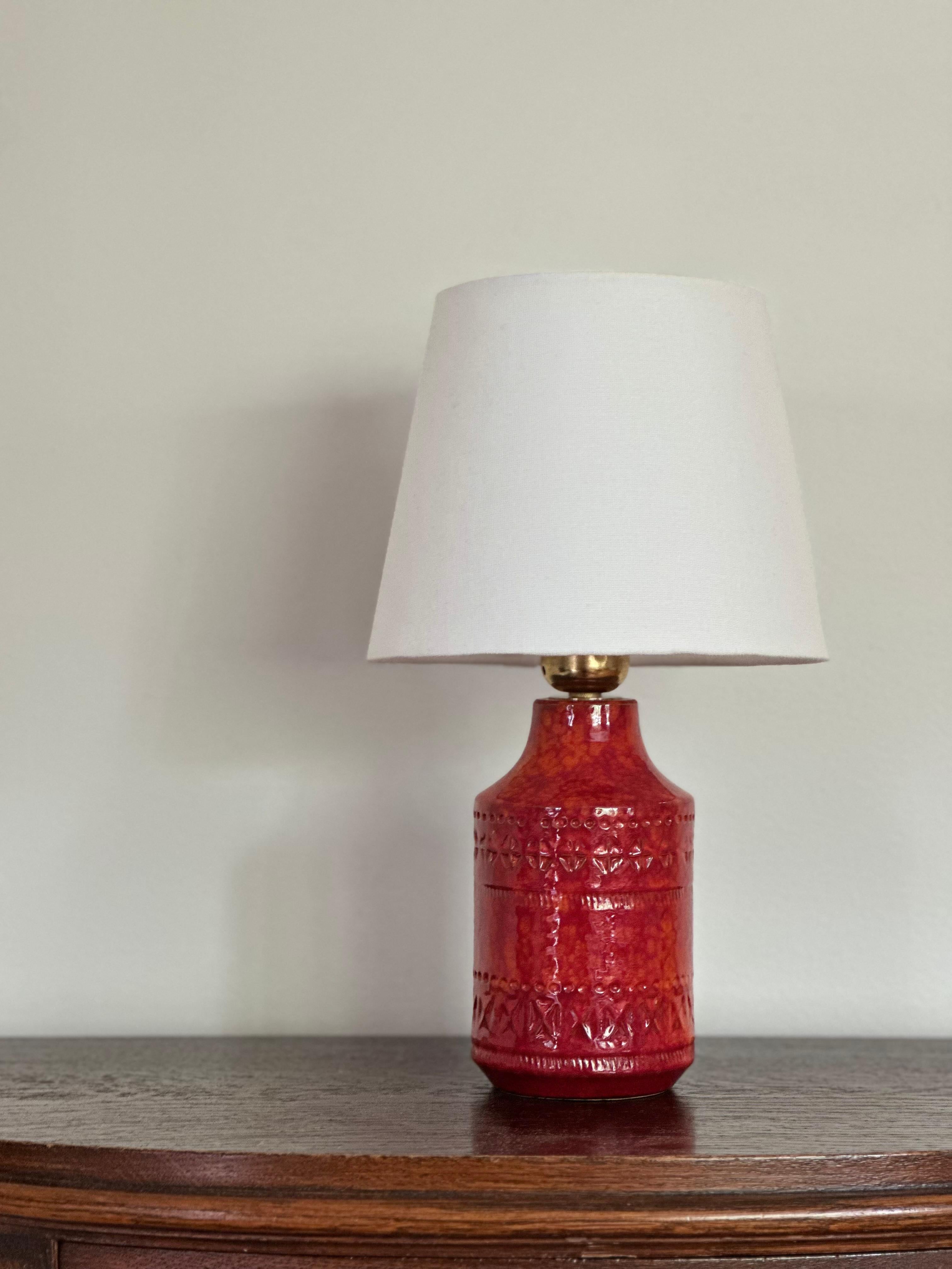 Lampe de table en céramique rouge colorée et audacieuse du milieu du siècle dernier. Le grès est jeté à la main dans les années 1960. Structure rugueuse avec une glaçure brillante rouge orangé.

Pied de lampe en poterie d'art dont le corps présente