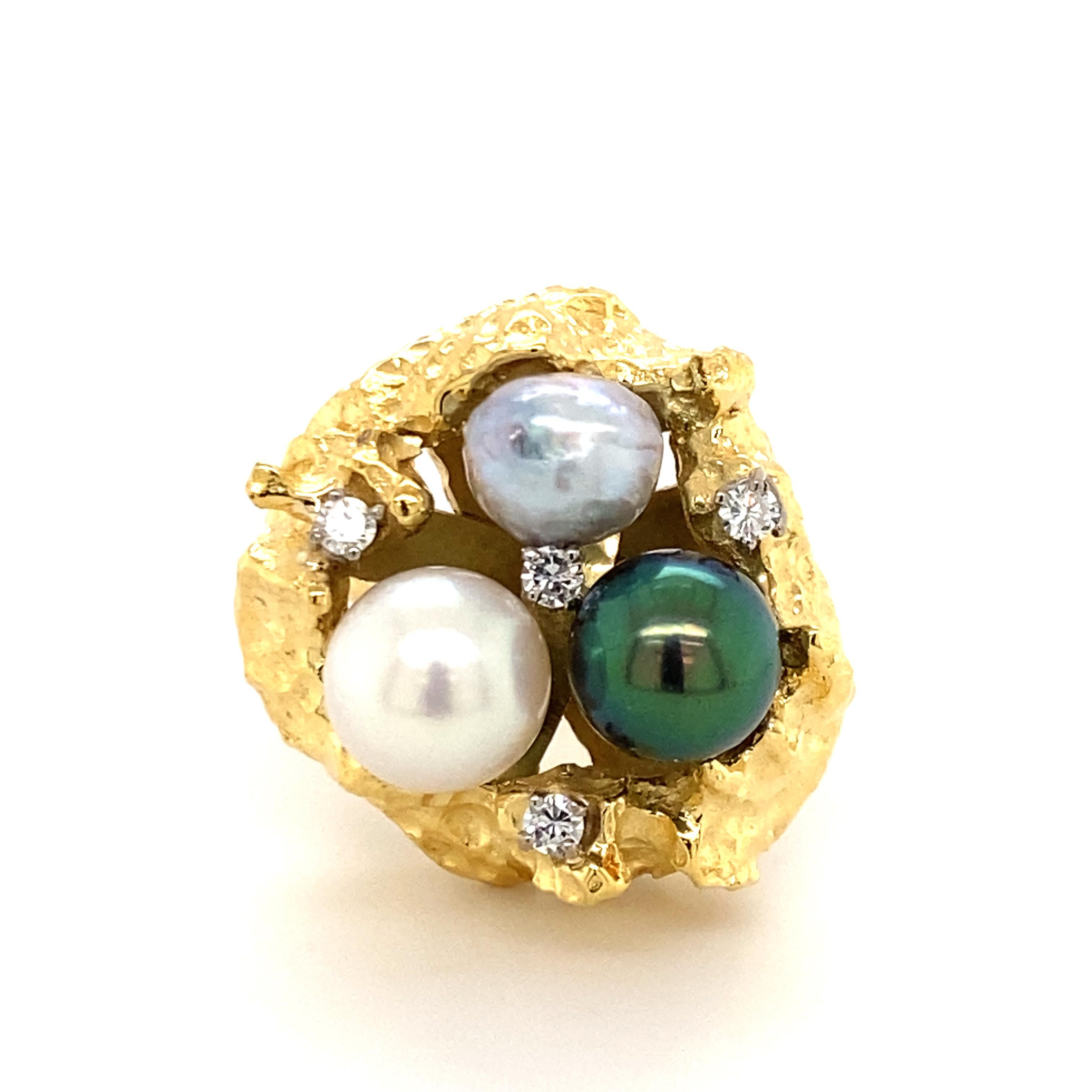 This stunningly chic ring in 14 karat yellow gold is set with three cultured pearls and four brilliant-cut diamonds. The vividly shimmering cultured pearls (white, green-grey and light grey, approx. 8.5 to 9.5 mm) are draped in a golden nest and