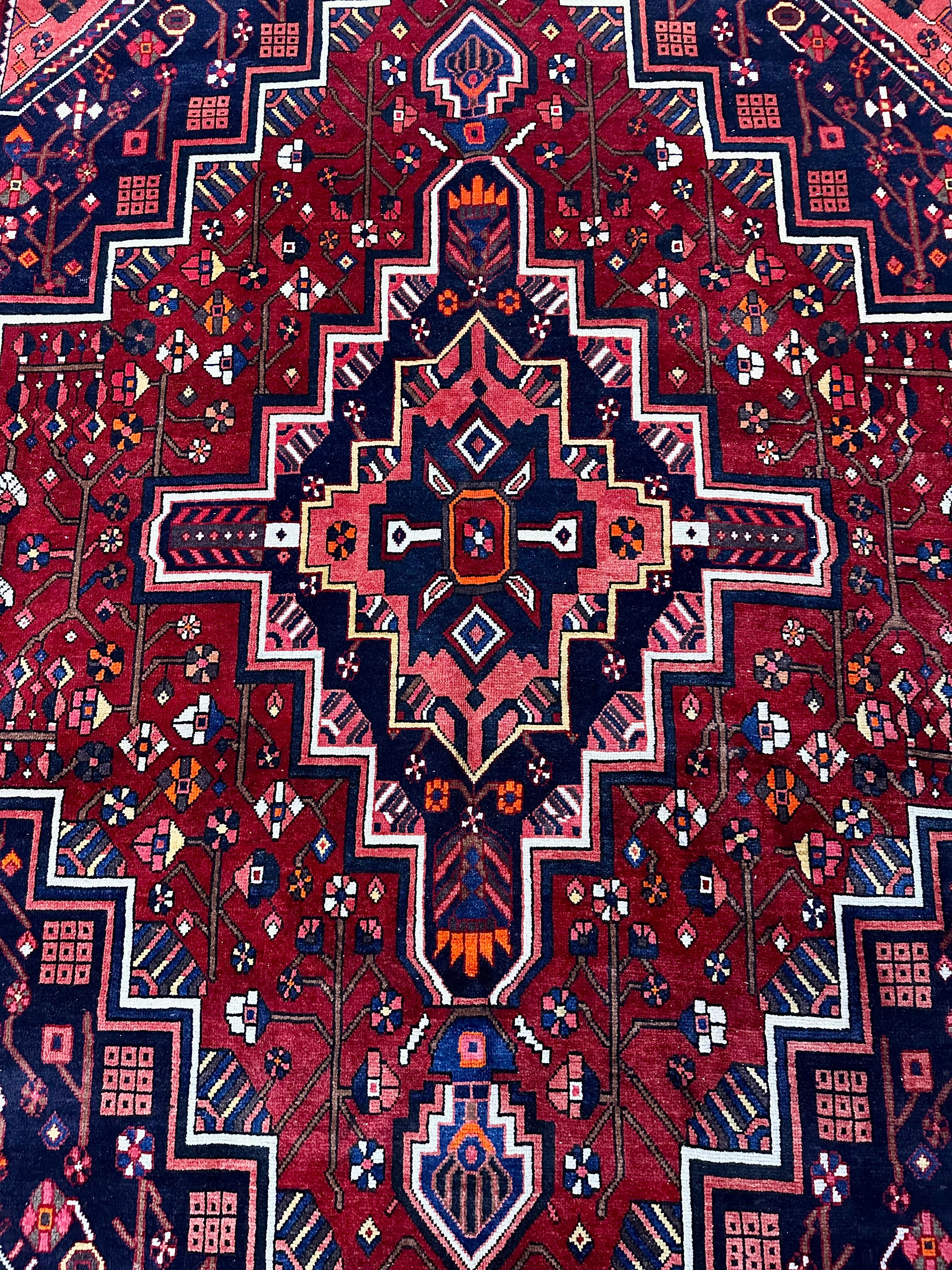 Vintage Persian Wool Hand Knotted Rug  9’L x 5.9’W. Sattes, kräftiges, rotes, geometrisches Blumenmuster im Tribal-Stil mit tiefem Marineblau, Weiß, Rosa, Orange und Gelb. Starkes und auffälliges Mittelmedaillon.

Geringfügige Vintage-Abnutzung,