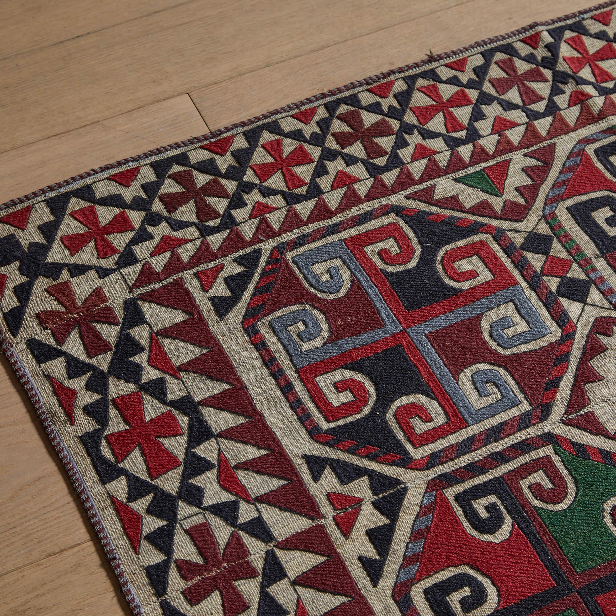 An early-twentieth century Uzbek tent hanging, boldly designed and meticulously embroidered in shades of red, blue, and green on a neutral, plain weave ground.
The large dynamic composition is made up of pieced panels to accommodate for the small