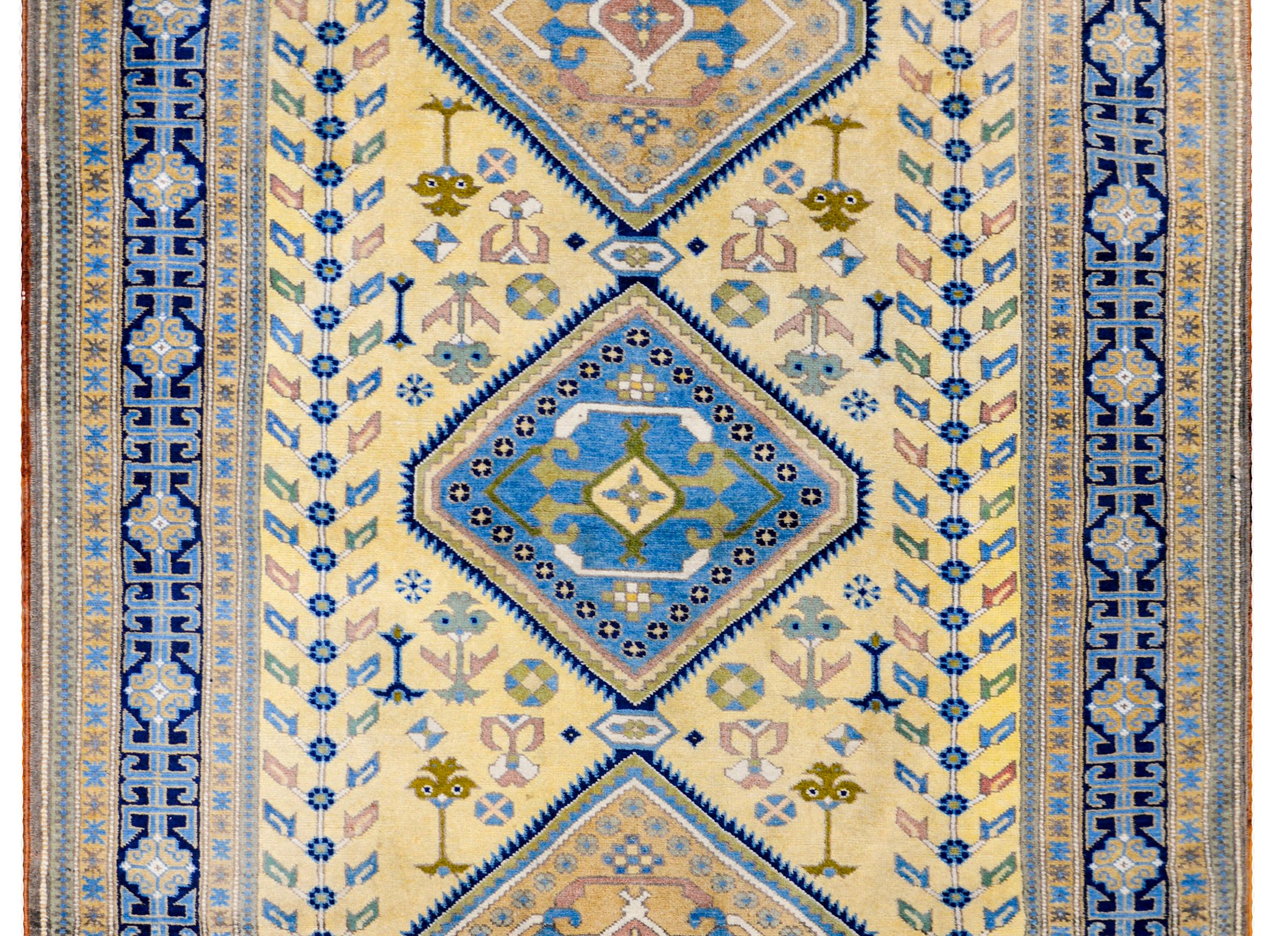 Tapis afghan kazakh de la fin du XXe siècle au design audacieux, avec trois grands médaillons centraux en forme de diamant sur un champ jaune pâle de fleurs stylisées et de grands arbres de vie flanqués de chaque côté. La bordure est magnifique avec