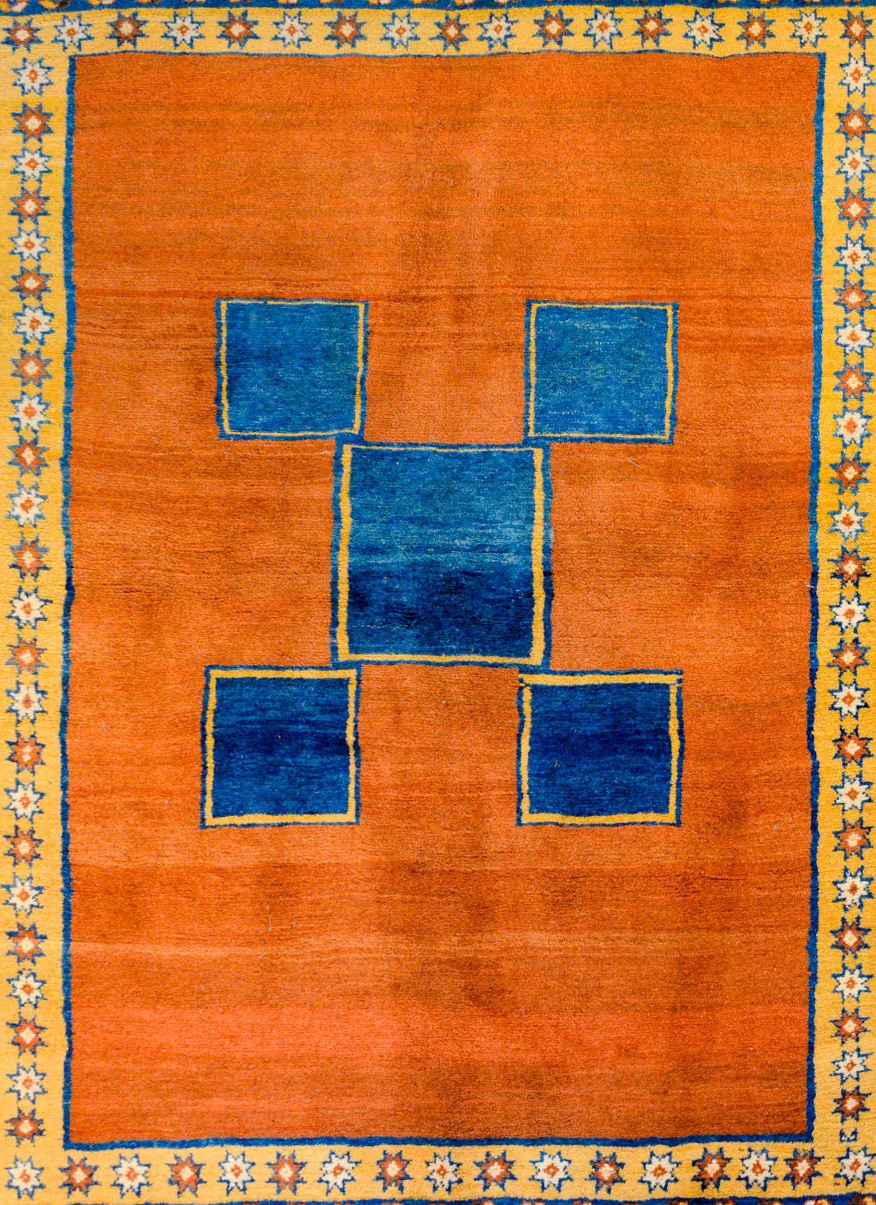 A bold vintage Persian Gabbeh rug with a five large indigo squares in the center of a rusty brown field surrounded by three patterned borders containing flowers and stripes, woven in orange, indigo, green, white, and gold.