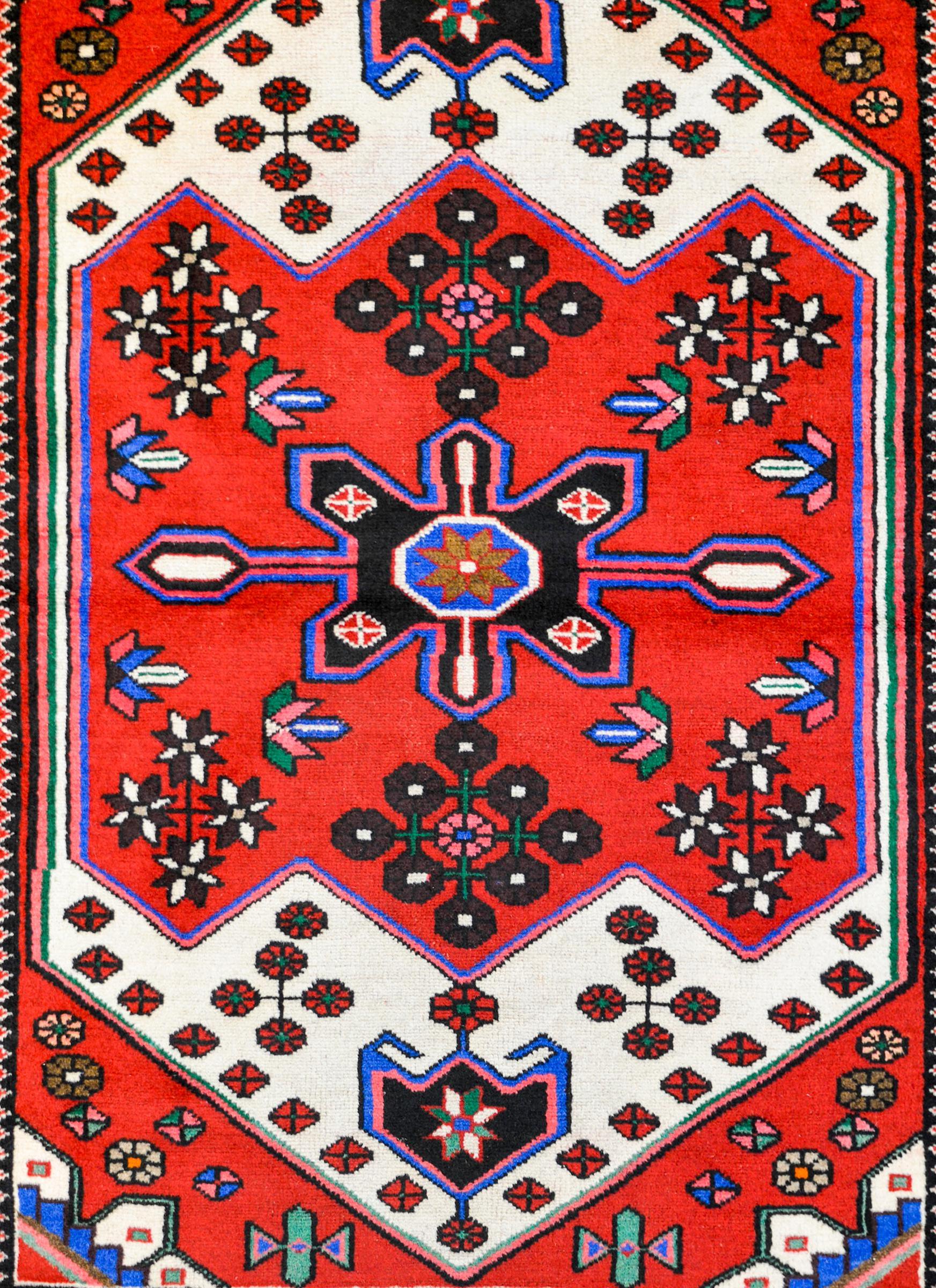 A vintage Persian Hamadan rug with myriad stylized flowers and clusters of flowers woven in white, brown, green, pink, and indigo on a bright crimson background. The border is simple with a petite flower and scrolling vine pattern flanked by petite