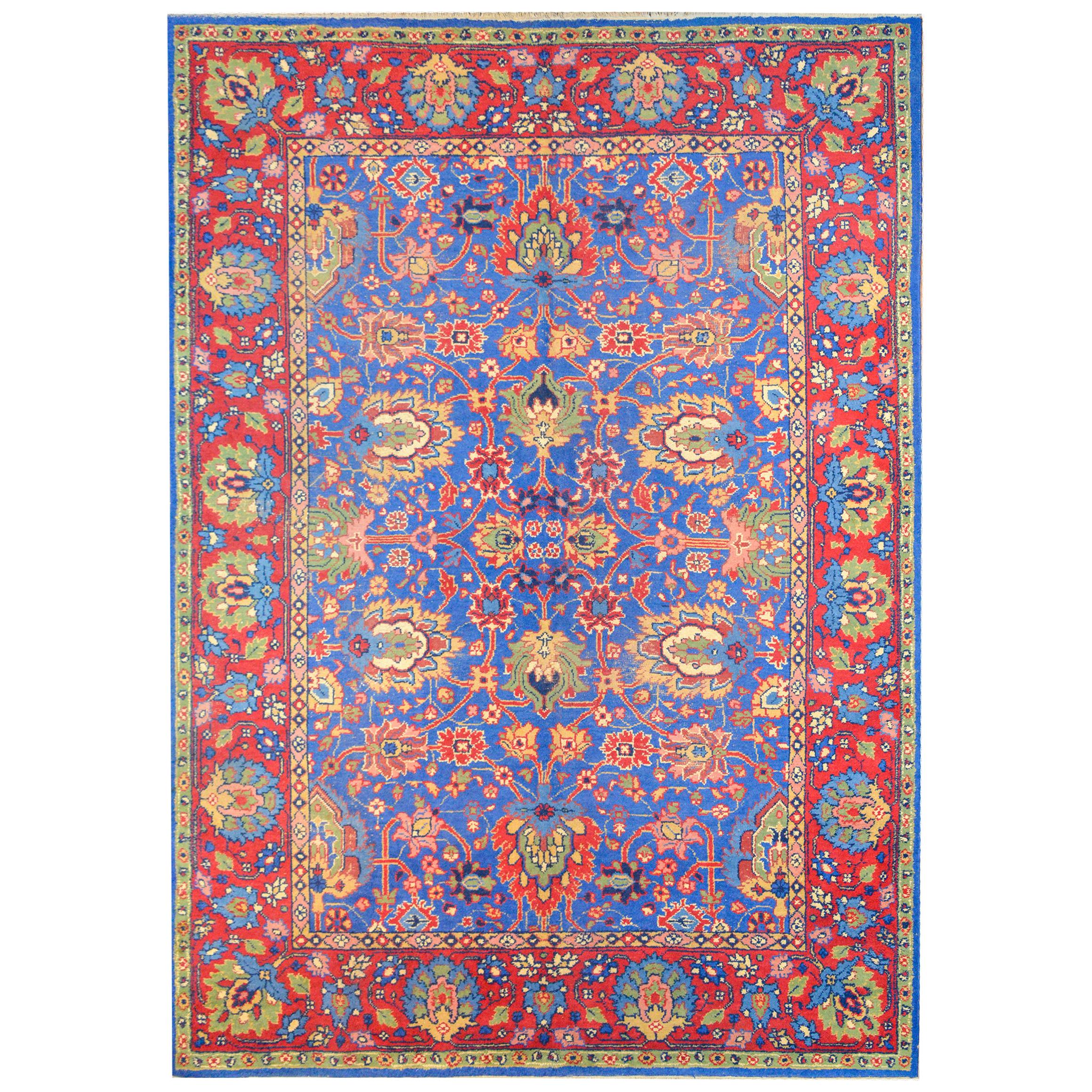 A bold vintage Persian mahal rug with an all-over large-scale floral and scrolling vine pattern woven in bright crimson, green, gold, cream, and indigo, against a light indigo background. The border is extraordinary with a wide central floral