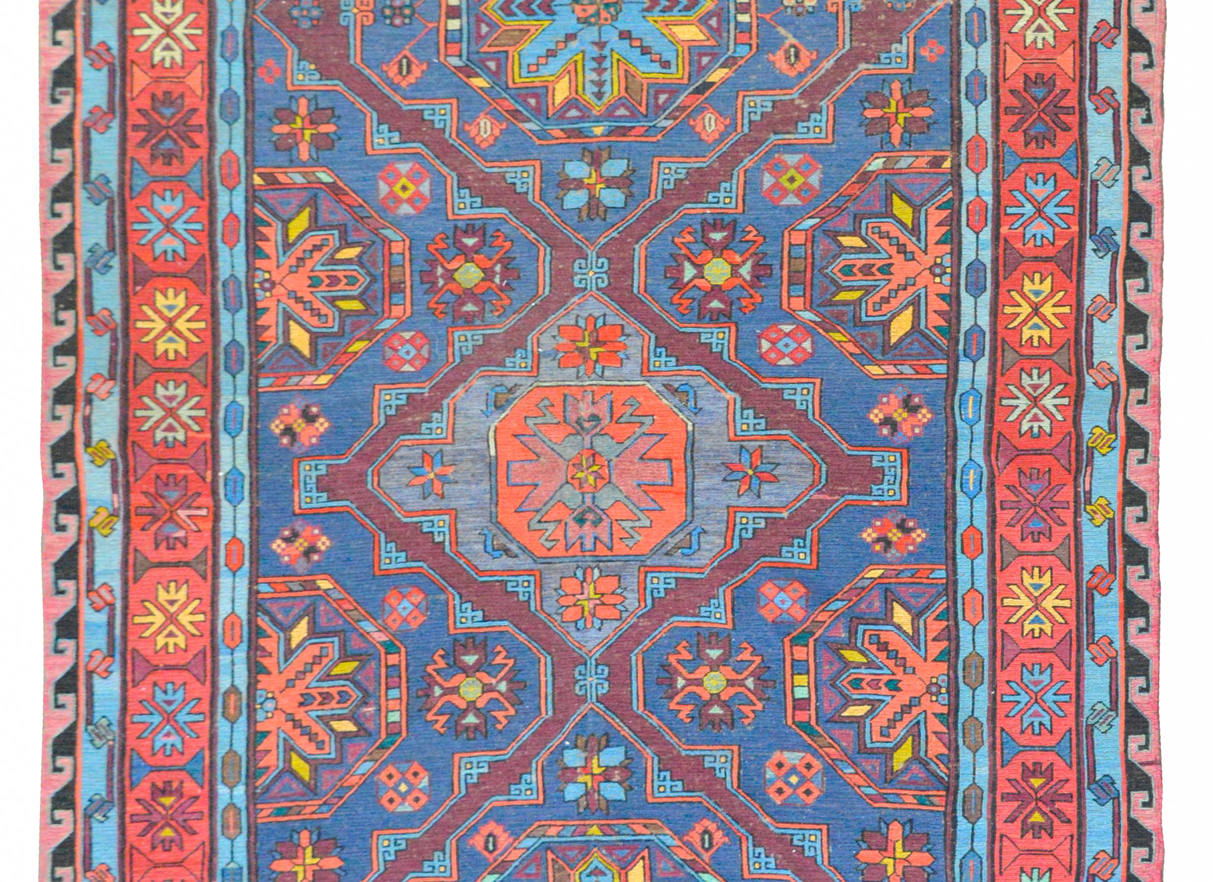 A fantastic bold vintage Afghani Soumak rug with three large diamond medallions with a stylized floral motif amidst a field of more stylized flowers, and all woven in coral, light and dark indigo, and violet. The border is complex, composed with