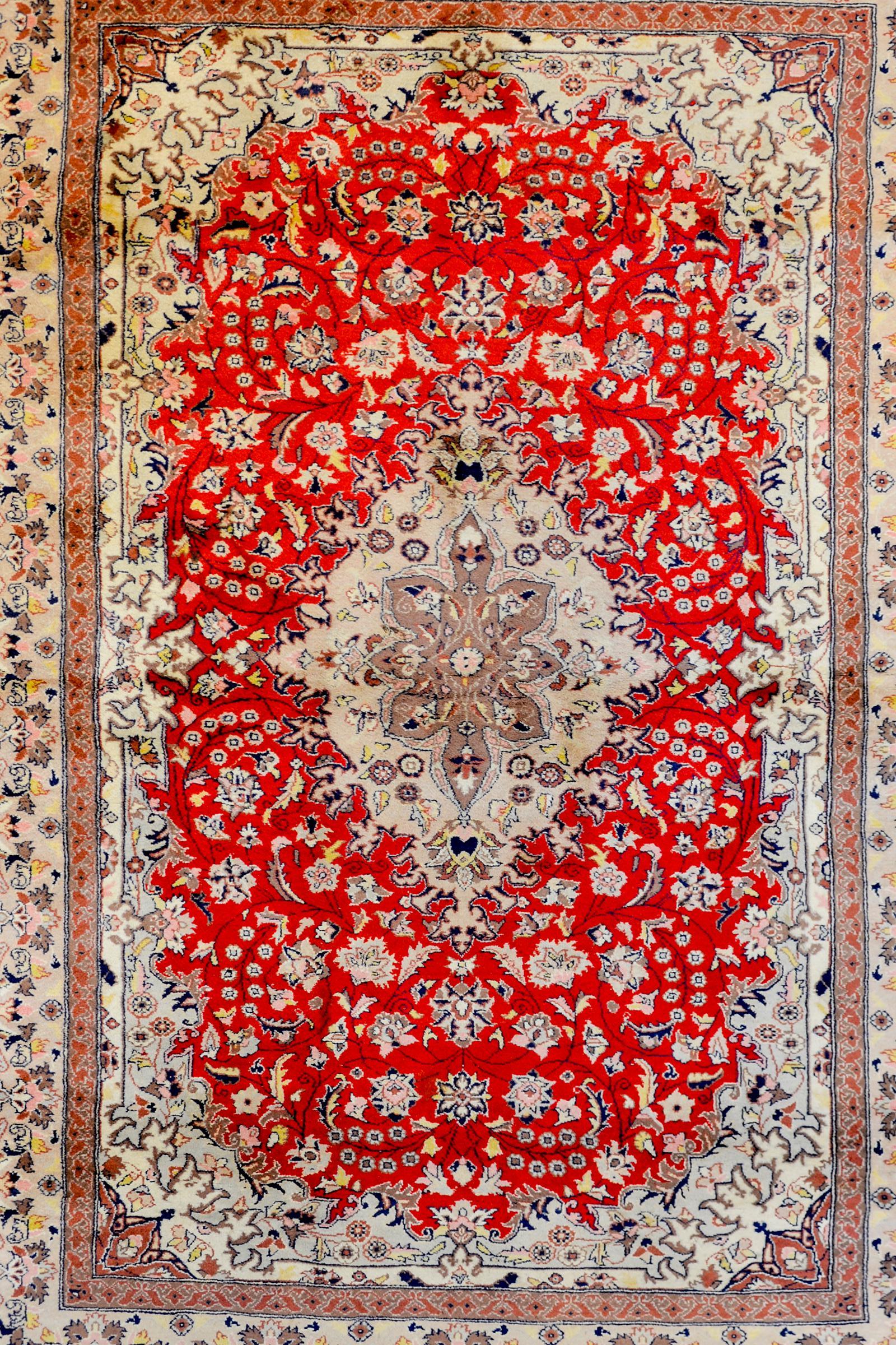 A bold vintage Chinese Tabriz-style rug with a large central floral medallion on a crimson field of scrolling vines, leaves, and flowers, surrounded by a wide floral and vine patterned border, flanked by pairs of matching petite floral patterned