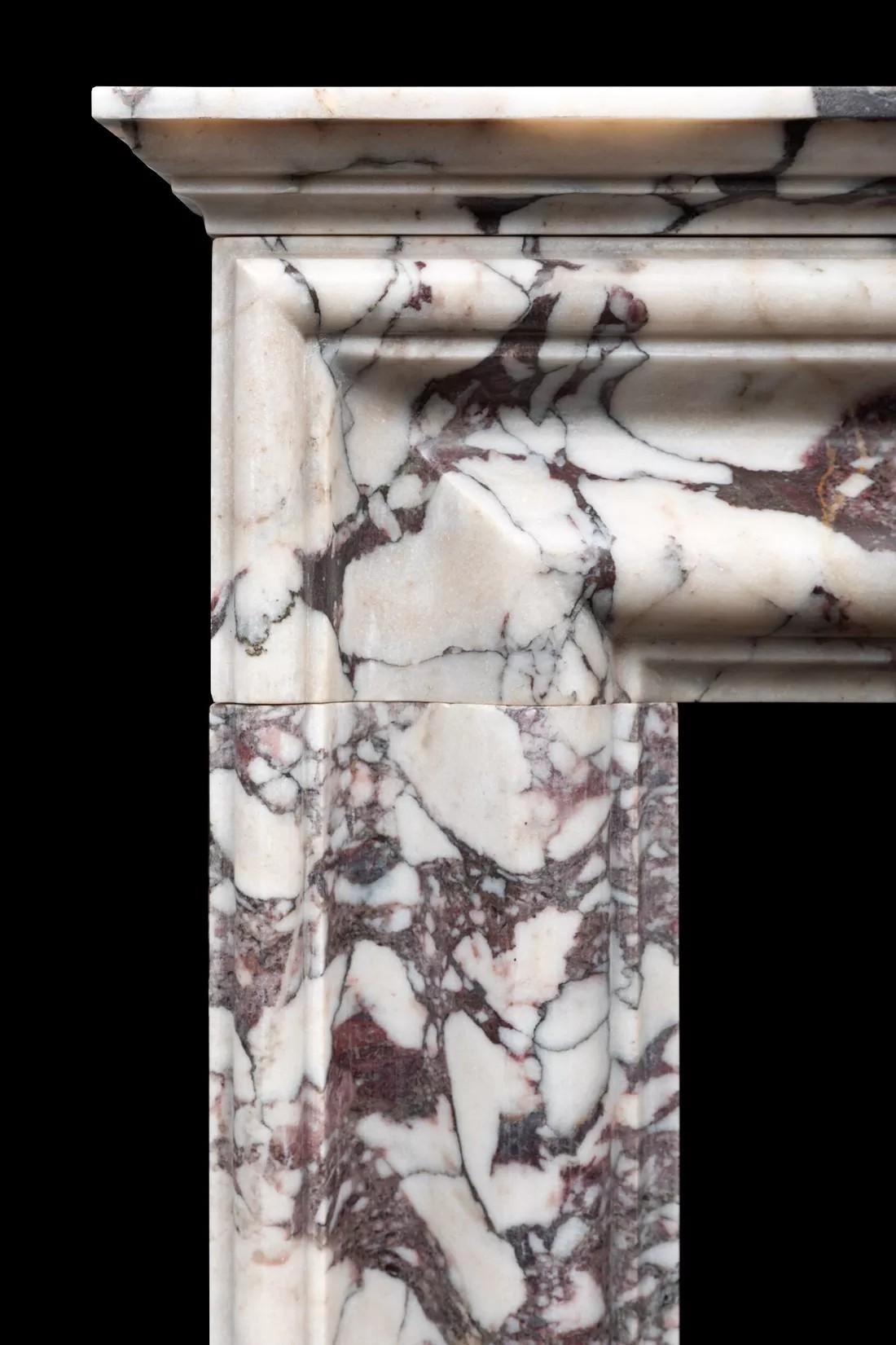 A stylish and neatly proportioned bolection fireplace produced in Italian Breccia Viola marble
The fireplace has a moulded bolection frame on plain plinths, with a stepped cornice shelf on top.

A classic design, fashionable in Europe for over three