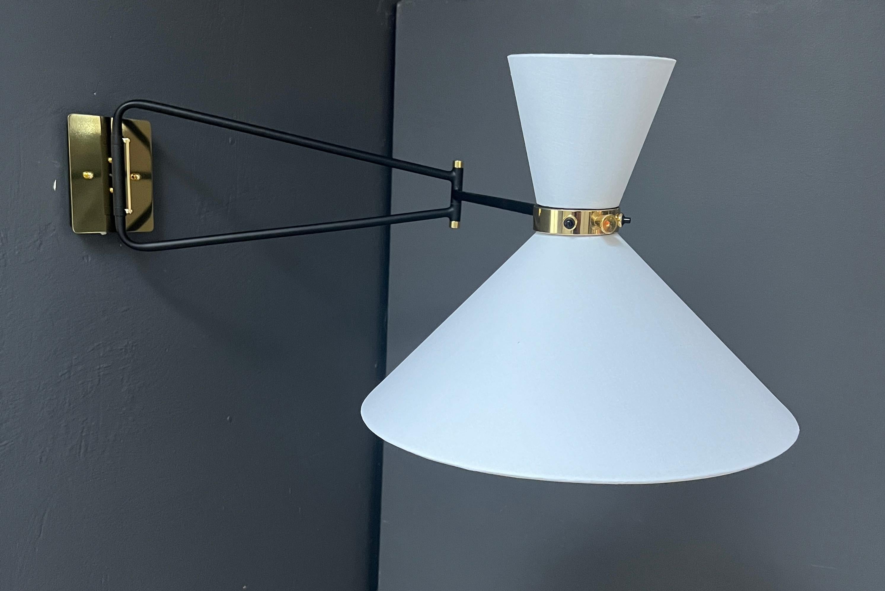 This sleek sconce is 1950s French midcentury by inspiration. The light with its double shade and articulated arm creates a versatile lighting source. The head pivots to direct the light of the two candelabra based bulbs in various direction while