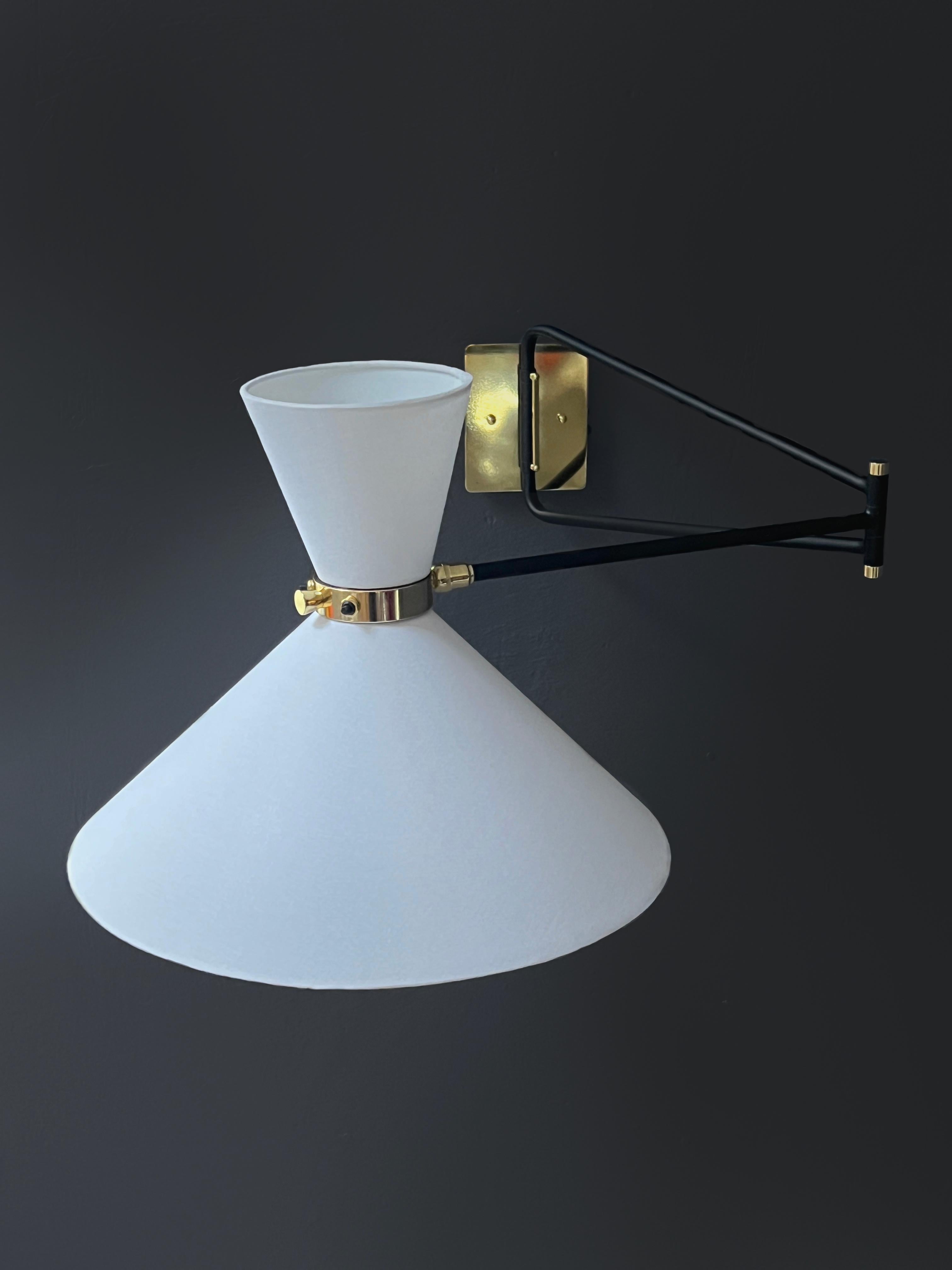 Questa elegante applique si ispira al midcentury francese degli anni Cinquanta. La lampada, con il suo doppio paralume e il braccio articolato, crea una fonte di illuminazione versatile. La testa ruota per dirigere la luce delle due lampadine a