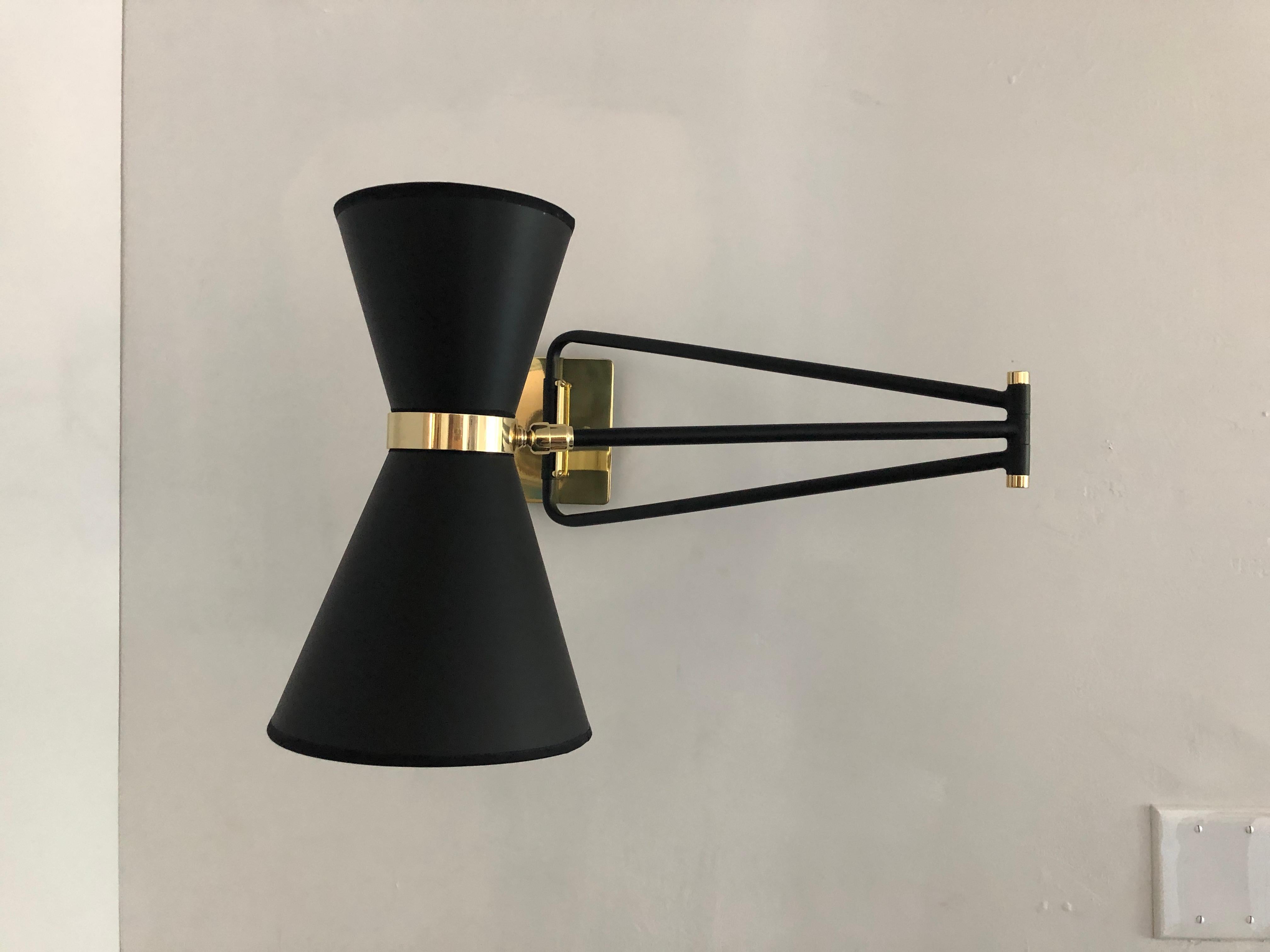 This sleek sconce is 1950s French midcentury by inspiration. The light with it double shade and articulated arm creates a versatile lighting source. The head pivots to direct the light of the two candelabra based bulbs in various direction while the