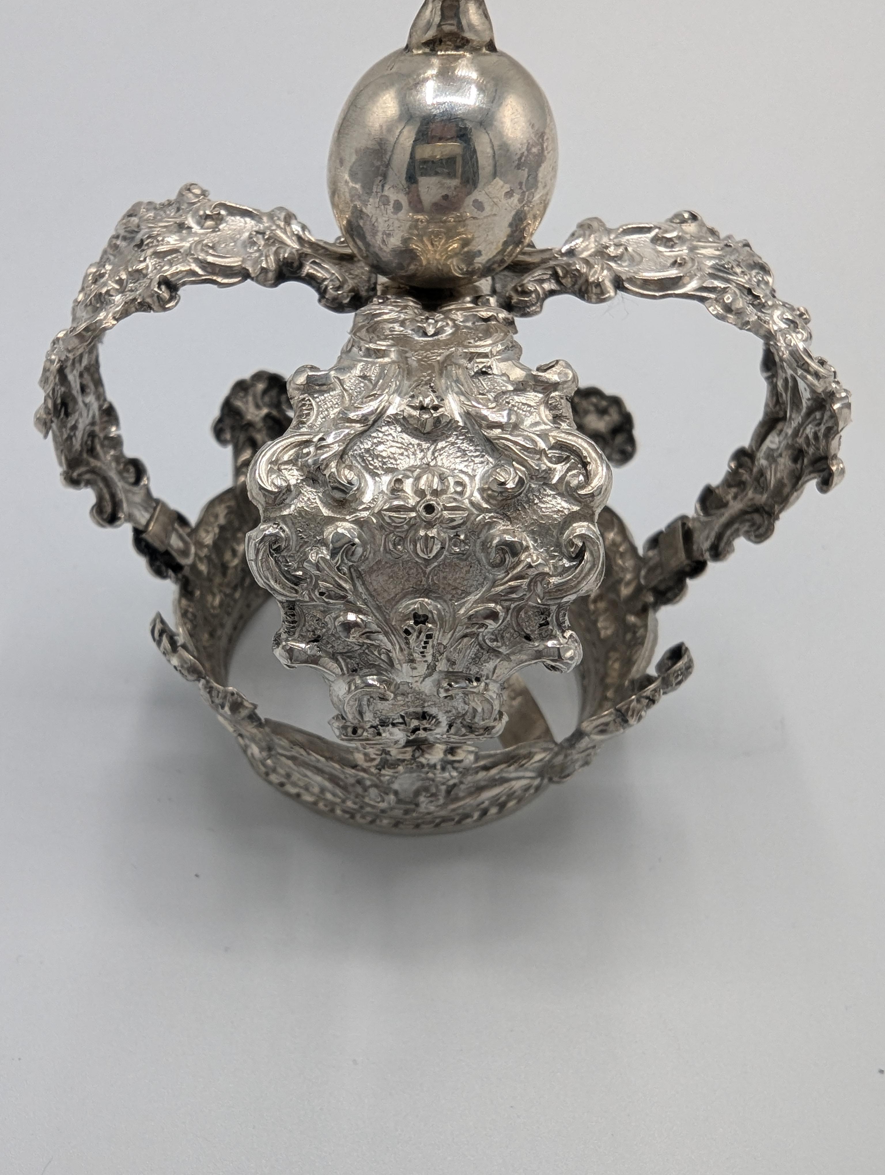 Cette couronne exquise en argent sterling témoigne d'un travail artisanal complexe et d'une élégance royale. Le design orné présente des fioritures détaillées de style baroque le long de la base, qui est habilement ornée de motifs à volutes et
