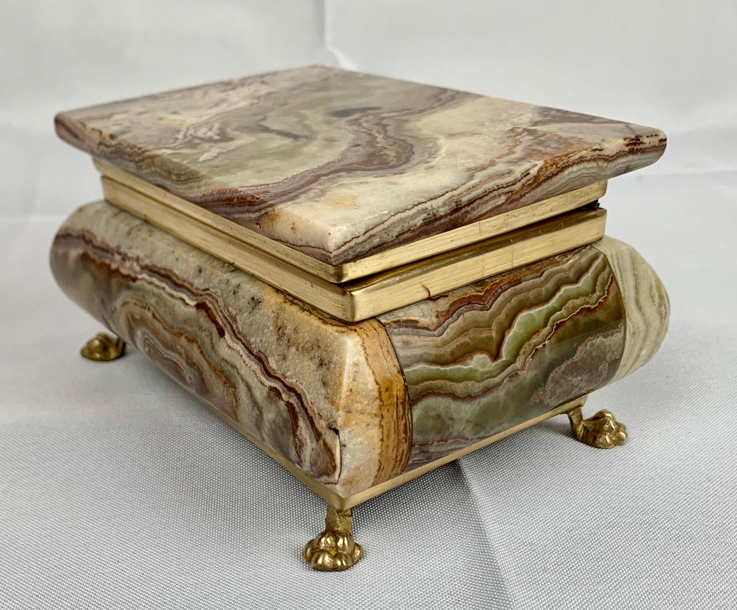 Beautifully marked natural onyx bombé shaped box with lion's paw feet. The hinged frame is brass.
The pieces of stone selected to make this box all have exotic markings. The lining is dark red velvet.
Measures: H-3