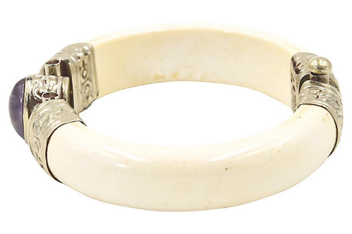 Bone bangle bracelet with silver-plated caps with raised floral design on the edges featuring a bezel set oval amethyst in the center. It has a pin closure. Interior 7