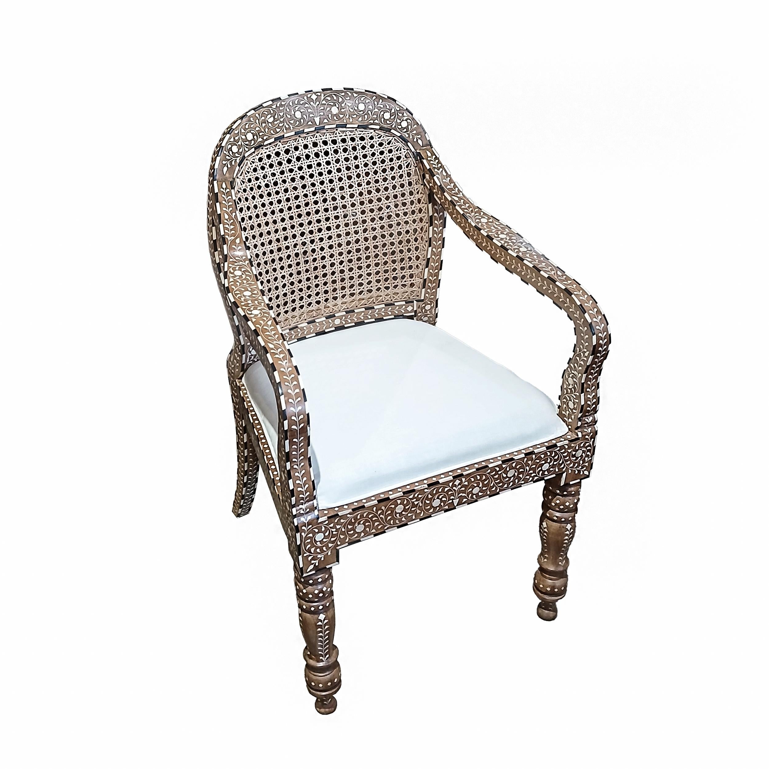 Una bellissima poltrona realizzata a mano in India con legno di teak invecchiato e stagionato naturalmente, intarsiato con osso di provenienza responsabile e canna intrecciata artigianalmente. Piano rotondo, schienale in canna, seduta imbottita e