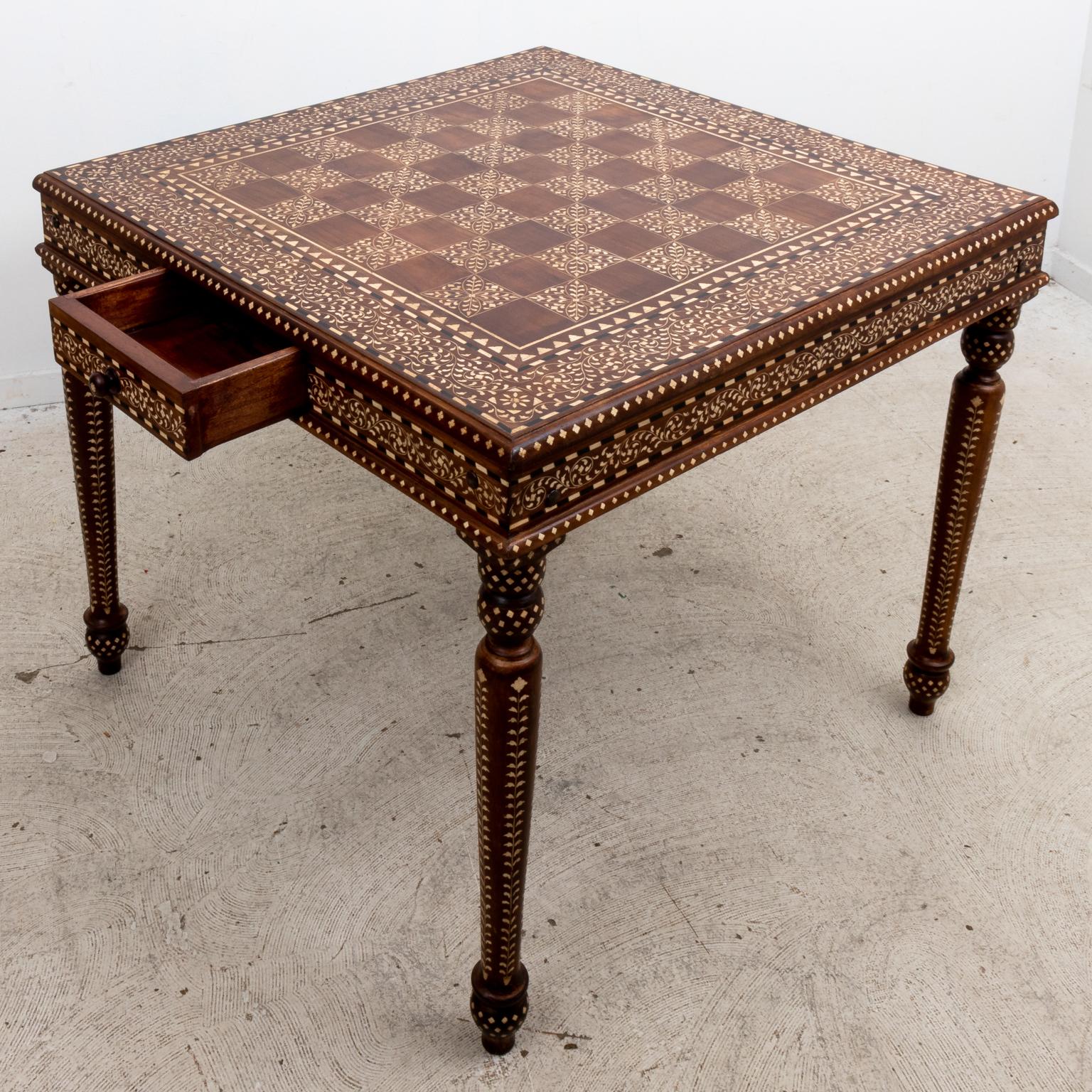 Camel bone inlaid card table with single horizontal drawer on arrow turned feet. The table is ornately inlaid throughout with decorative trim in patterns such as scrolled foliage, black-and-white stripes, and diamonds. On the tabletop is large