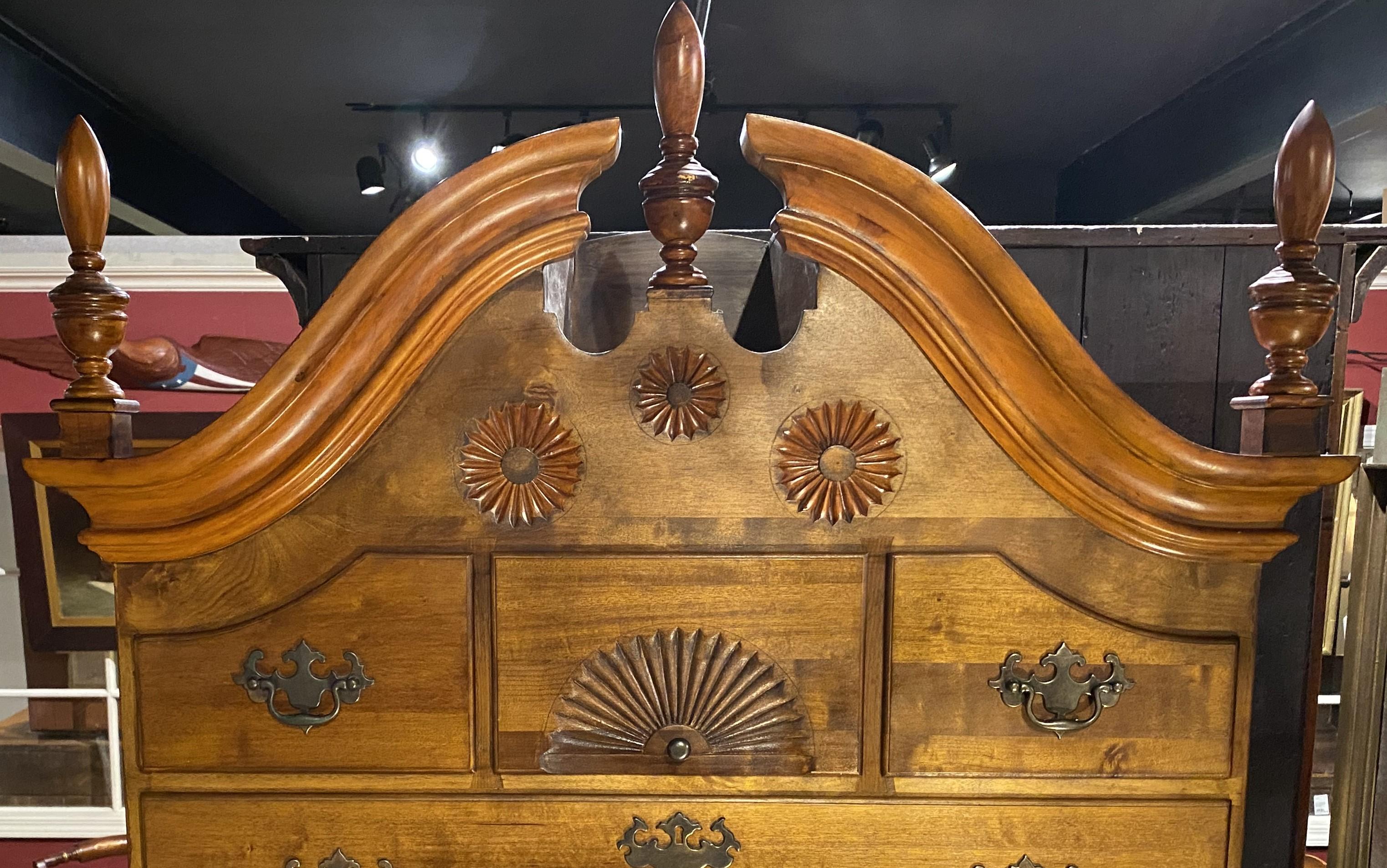 A Queen Anne style bonnet top highboy with swan’s neck split pediment with urn form finials surmounting an upper case with three pinwheel carvings over three fitted drawers, the central drawer featuring a radial fan carving, over four long drawers,