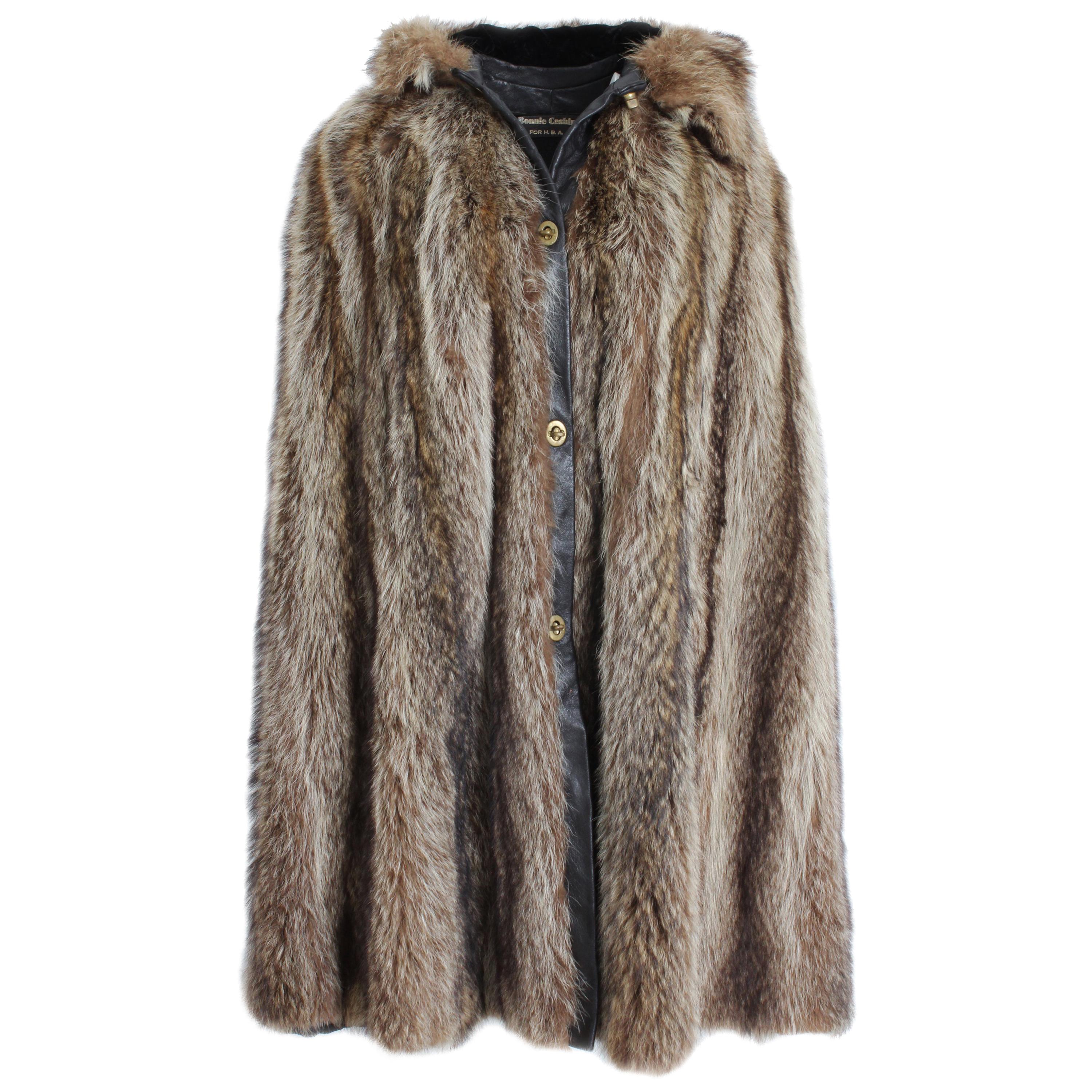 Exquisite Bonnie Cashin for HBA Furs Hooded Raccoon Fur Cape, circa 1974.  Lined in black fabric, it fastens with Bonnie's signature brass turn locks and is trimmed in brown leather.  Arm holes feature hidden interior pockets.  

An iconic hooded