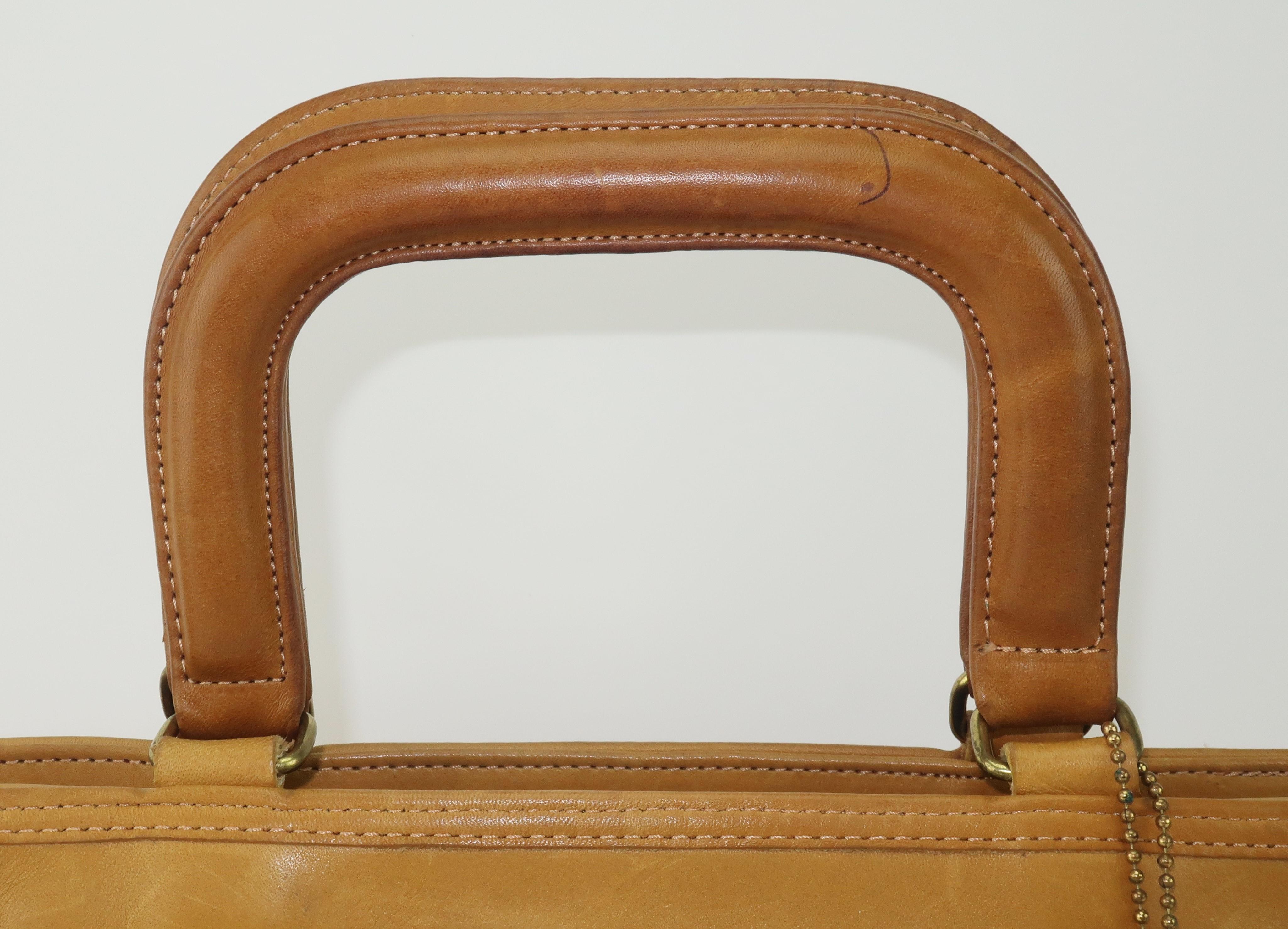1970's tan leather Coach handbag originally designed by Bonnie Cashin and nicknamed the Watermelon tote.  The handbag has the practical silhouette of a top handle briefcase with a zipper closure which opens to reveal a roomy interior and a fun outer