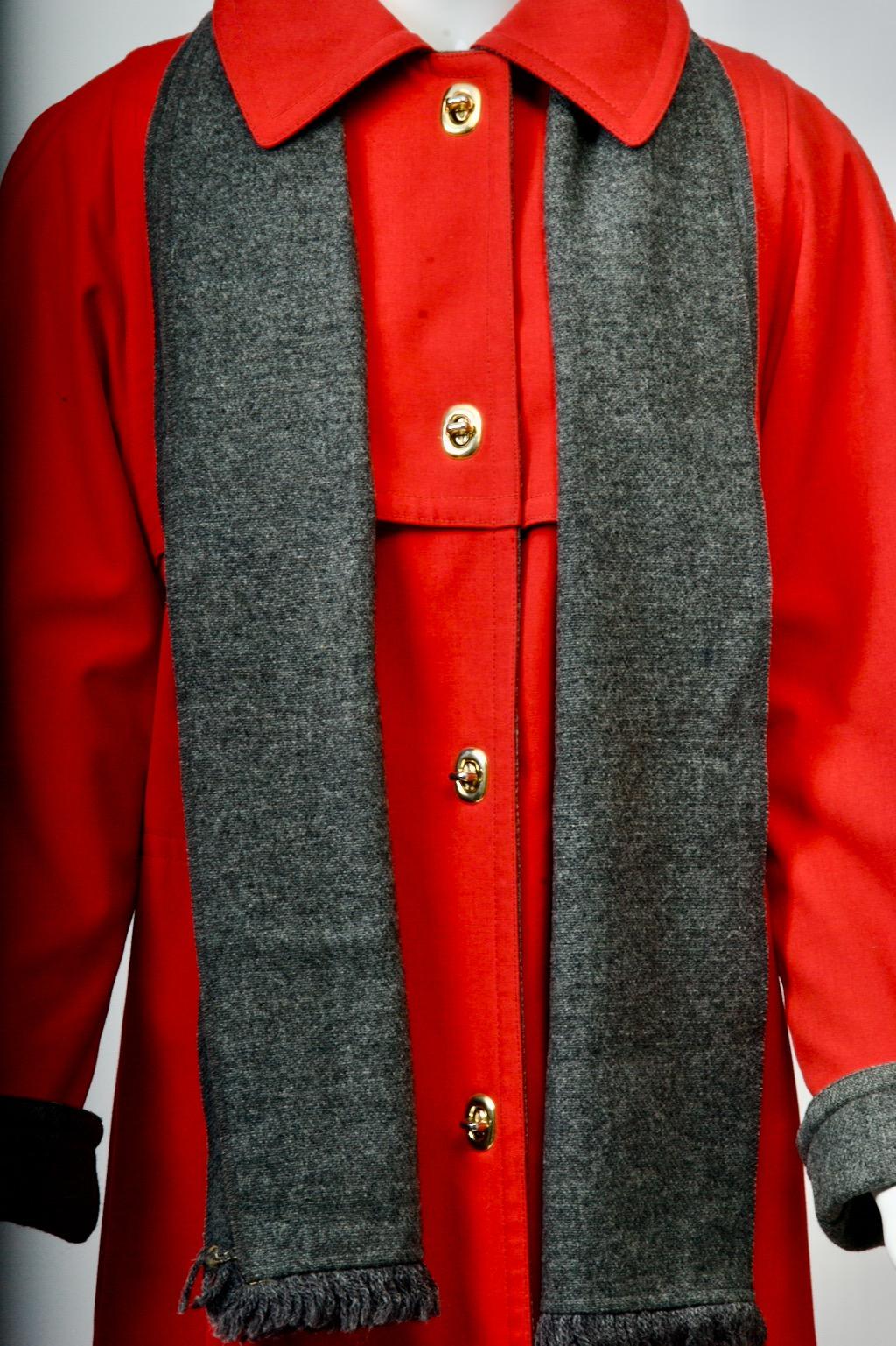 An original c.1970s Bonnie Cashin all-weather coat in red poplin, lined in charcoal wool, and with attached charcoal wool scarf. The coat features Cashin's signature toggle closures and has yoke detailing front and back. Side slit pockets. Cuffs can