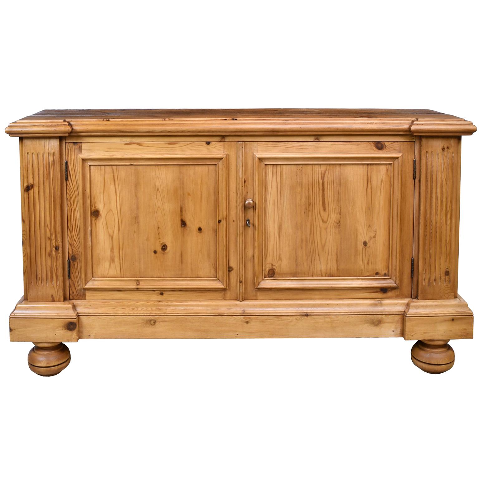 A sideboard or credenza in reclaimed antique European pine with fluted pilasters flanking two cabinet doors with recessed panels that open to a storage space with a shelf. The sides also have a recessed panel. A classically-inspired, Bonnin Ashley