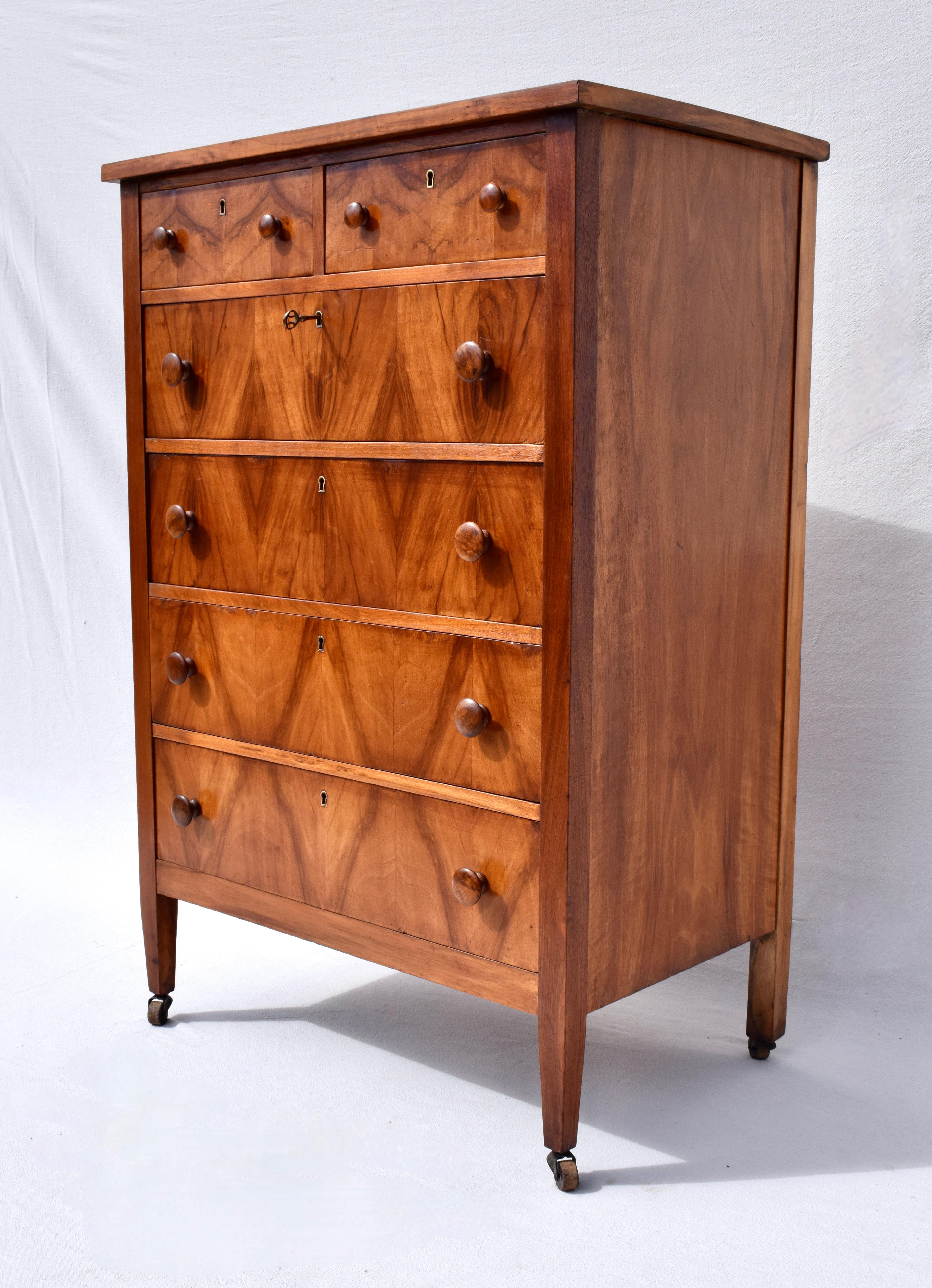 A mid sized highboy chest of six drawers boasting an impressive show of book matched flame Mahogany wood grains with working locks on all drawers and key. Fully refinished, the chest is quite substantial and solid perched on original casters.