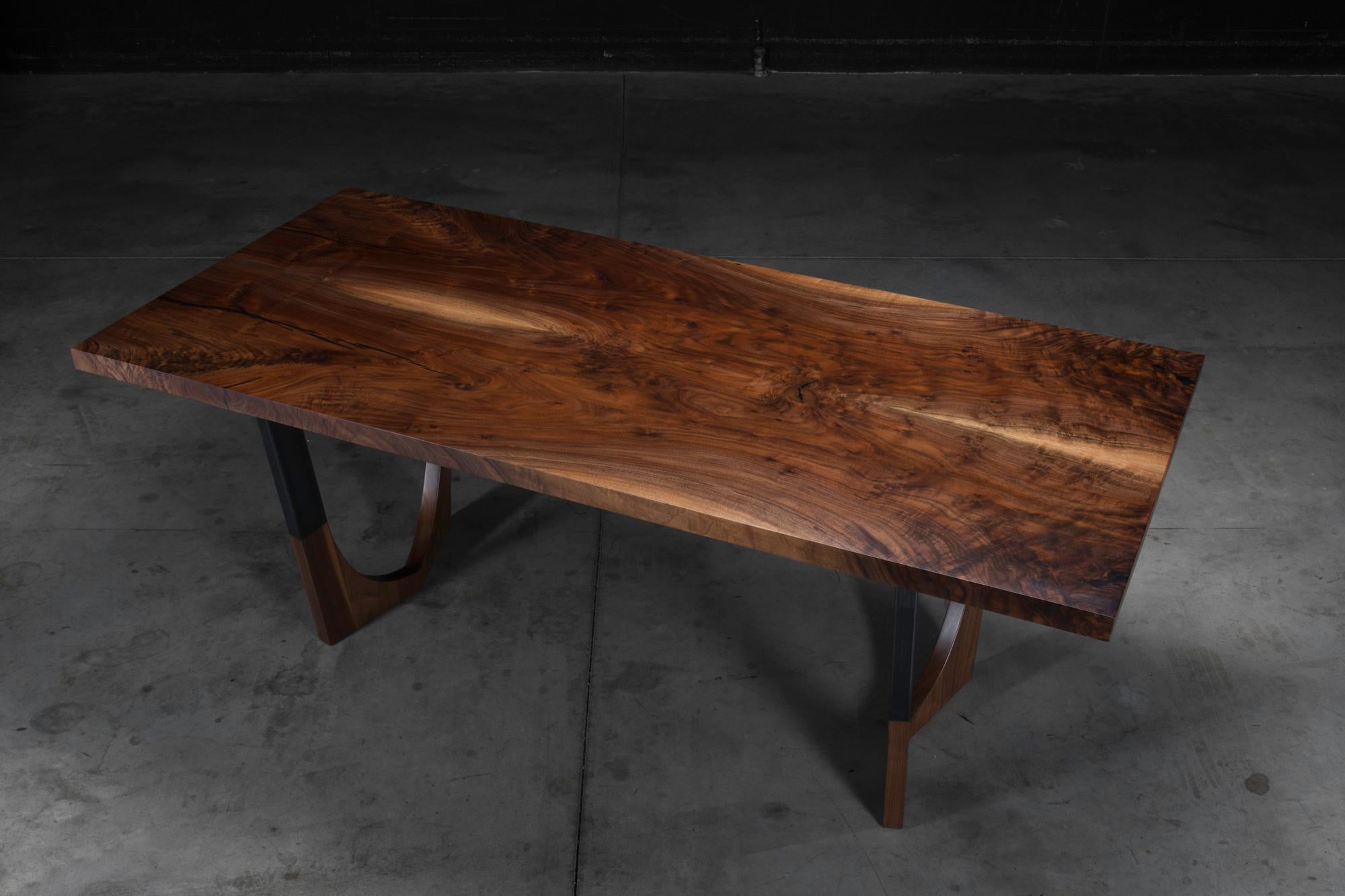 The Lafayette dining table is made of a book-matched claro walnut top with a blackened steel base with walnut inserts. This piece has been finished in an extremely durable matte conversion varnish. The dark tone of the claro walnut top is brought