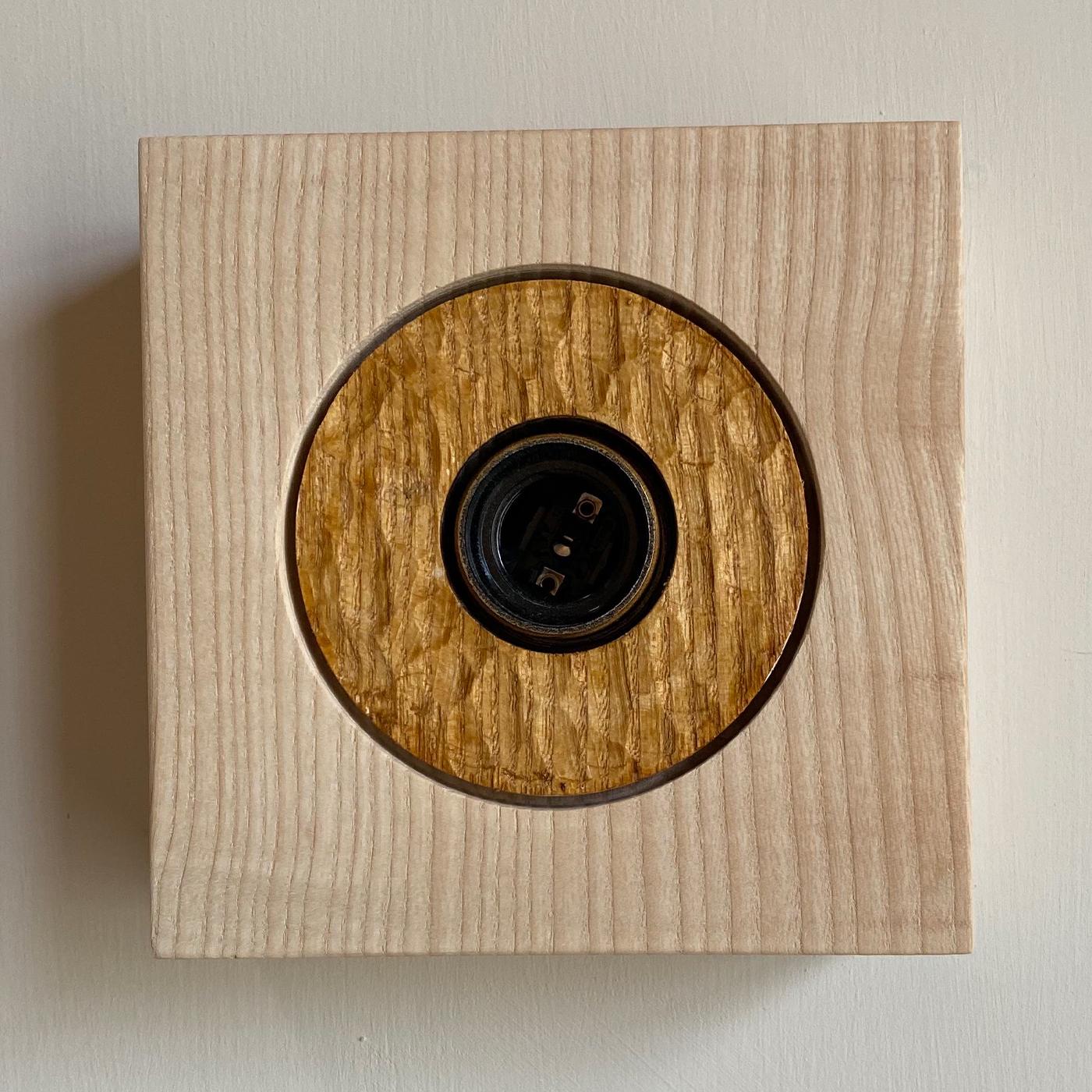 Part of the Book Collection, this ashwood wall lamp is designed by Tuscany-based artist Pietro Meccani and crafted using exclusively natural, non-toxic materials. Carved and finished by hand in stained oak, the circle within the square frame
