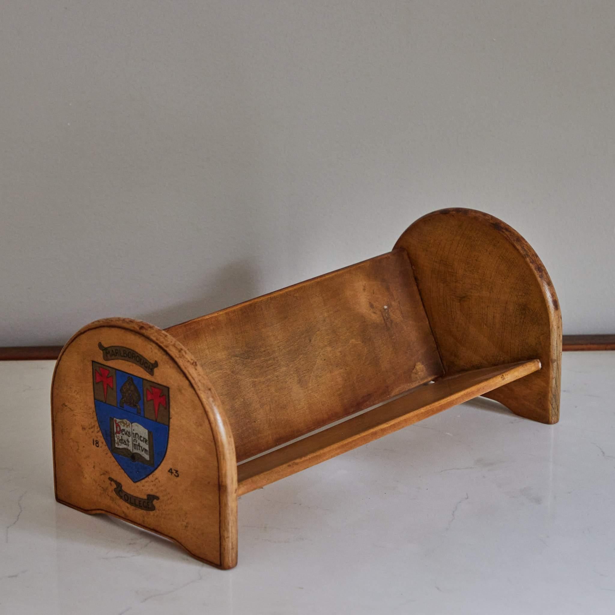 Early 20th-century book shelf from an English boarding school. Charming and conveniently scaled, the shelf features a hand-painted Marlborough College crest on either of its sides. With the soft blond patina of wood and cozy scholastic feel, this