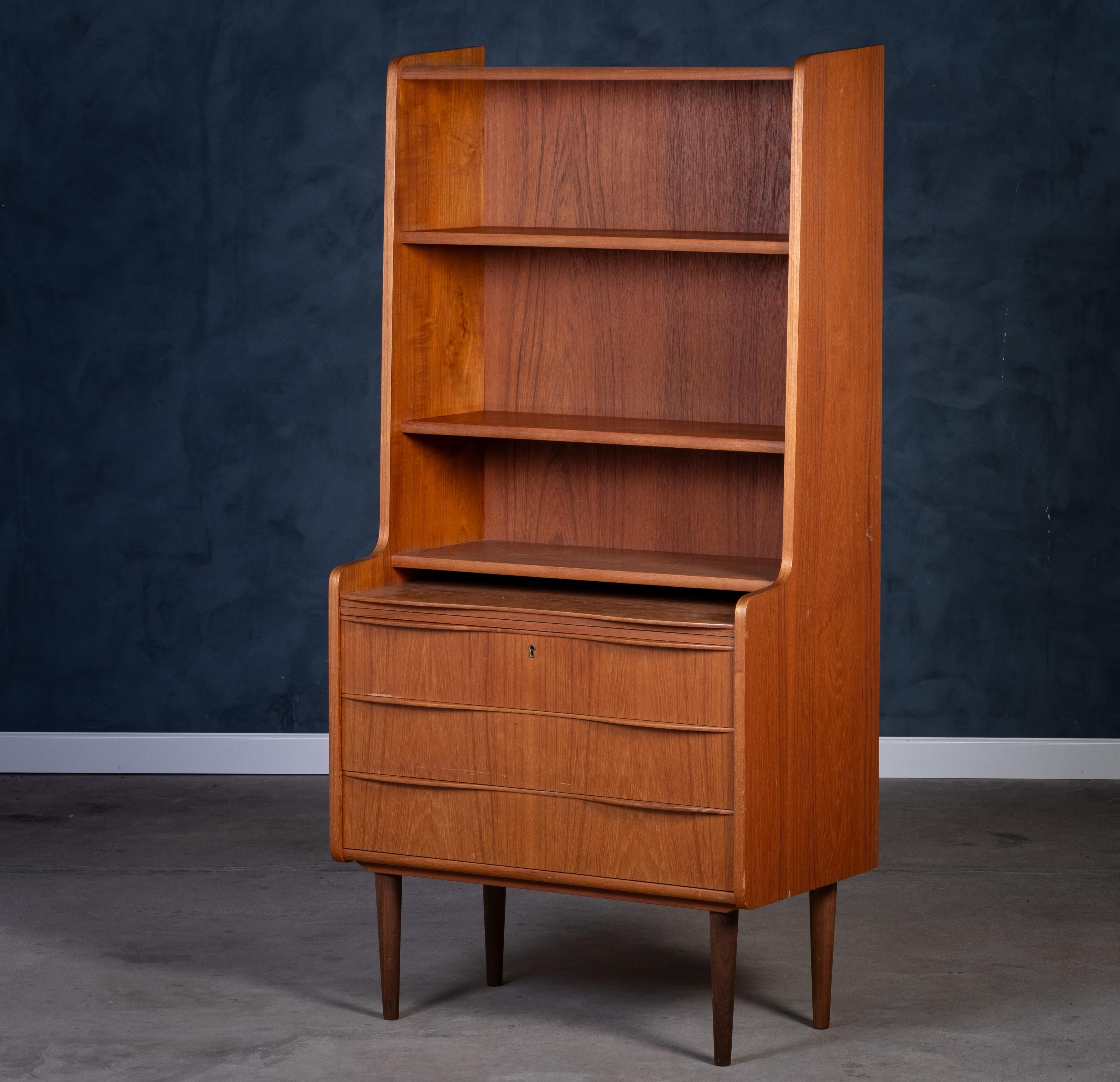 Bellissima libreria danese degli anni '60 realizzata in caldo legno di teak. Dispone di tre spaziosi cassetti con eleganti maniglie e di scaffali aperti per esporre o riporre oggetti. Un pezzo di design senza tempo della metà del secolo scorso che