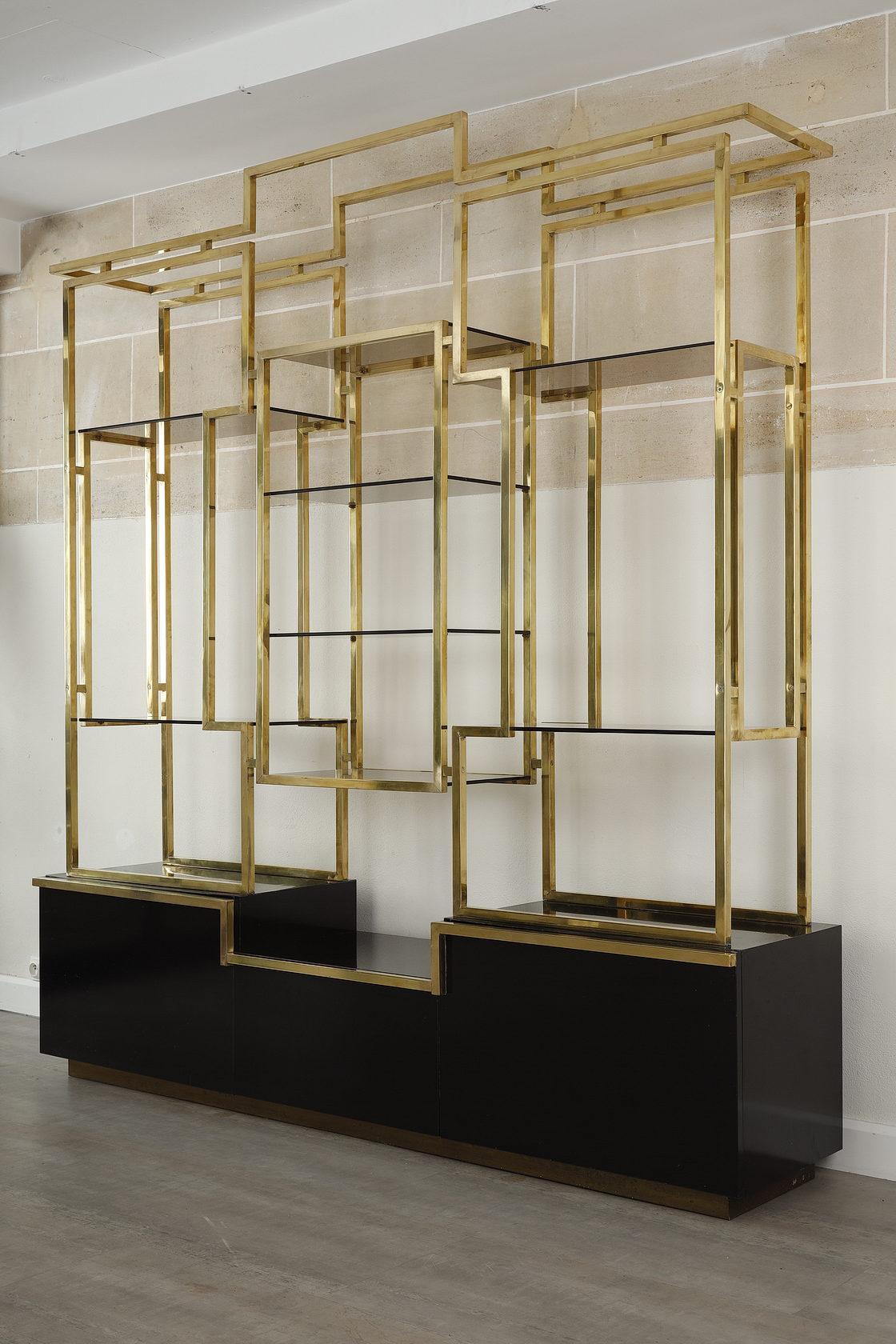 Large design bookcase by Kim Moltzer made in the 1970s. The bookcase is rectangular in shape and uses the geometric forms favoured by the designer. It has eight smoked glass shelves in a large gilded brass structure. The black lacquered wooden base