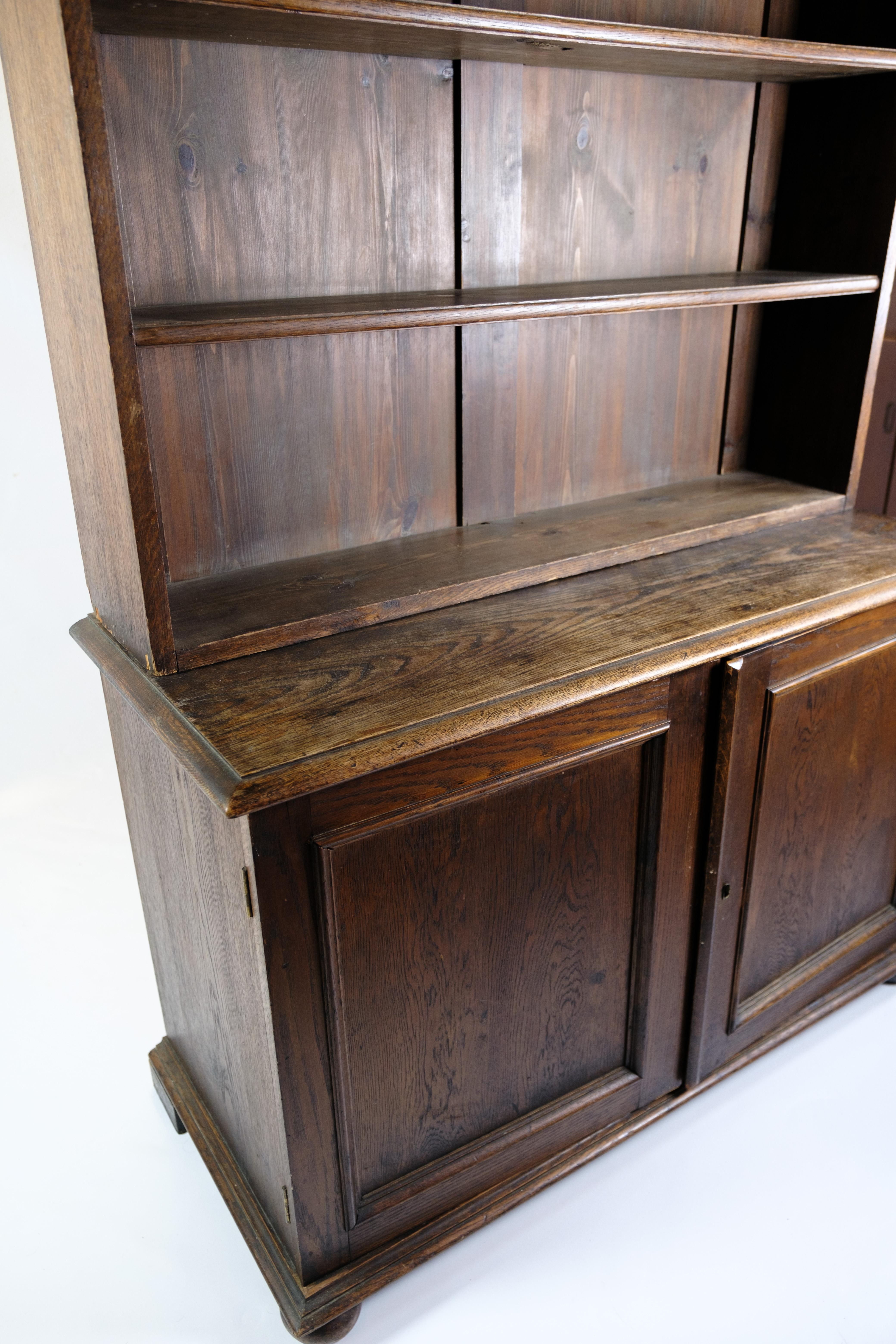 This tall bookcase in oak from 1890 year is an exemplary piece of furniture craftsmanship with both elegance and functionality. It is equipped with a lower sideboard with two cabinet doors and a bookcase with six shelves, providing ample storage
