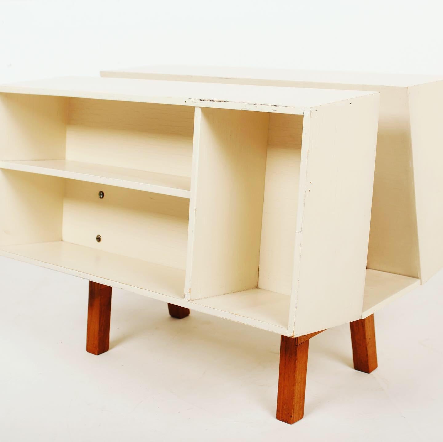 The bookcase Penguin Donkey Mark 2 was designed in 1963 after Jack Pritchard asked to Ernest Race to reconfigure Egon Riss's original design to include a flat top that would allow it to be used as a side table. White painted wood with legs in cherry
