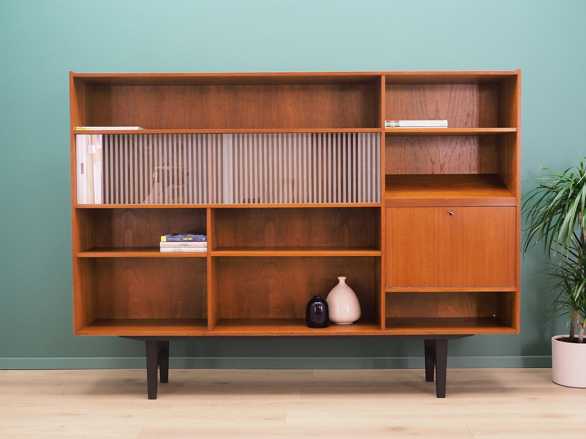 Bookcase was made in the 1970s, Danish production.

The structure is covered with teak veneer. Legs made of solid wood stained black. Surface after refreshing. Inside the space has been filled with practical shelves. The shelves are not adjustable