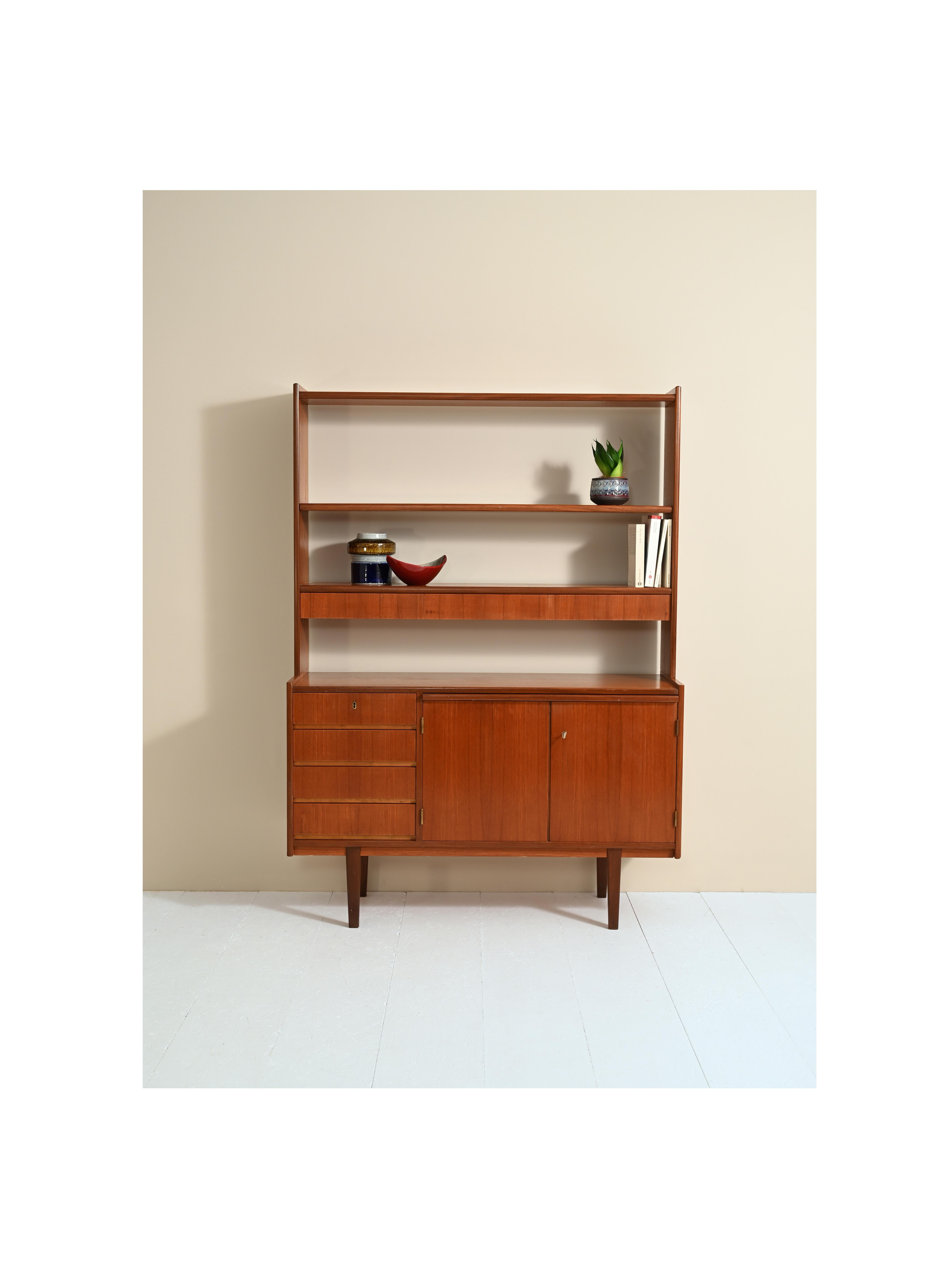 Danish teak cabinet from the 1960s.
The upper part of the bookcase has an adjustable-height shelf and a shelf with drawers. The lower part is a proper sideboard with drawers and a storage compartment. There is also a pull-out shelf that is useful