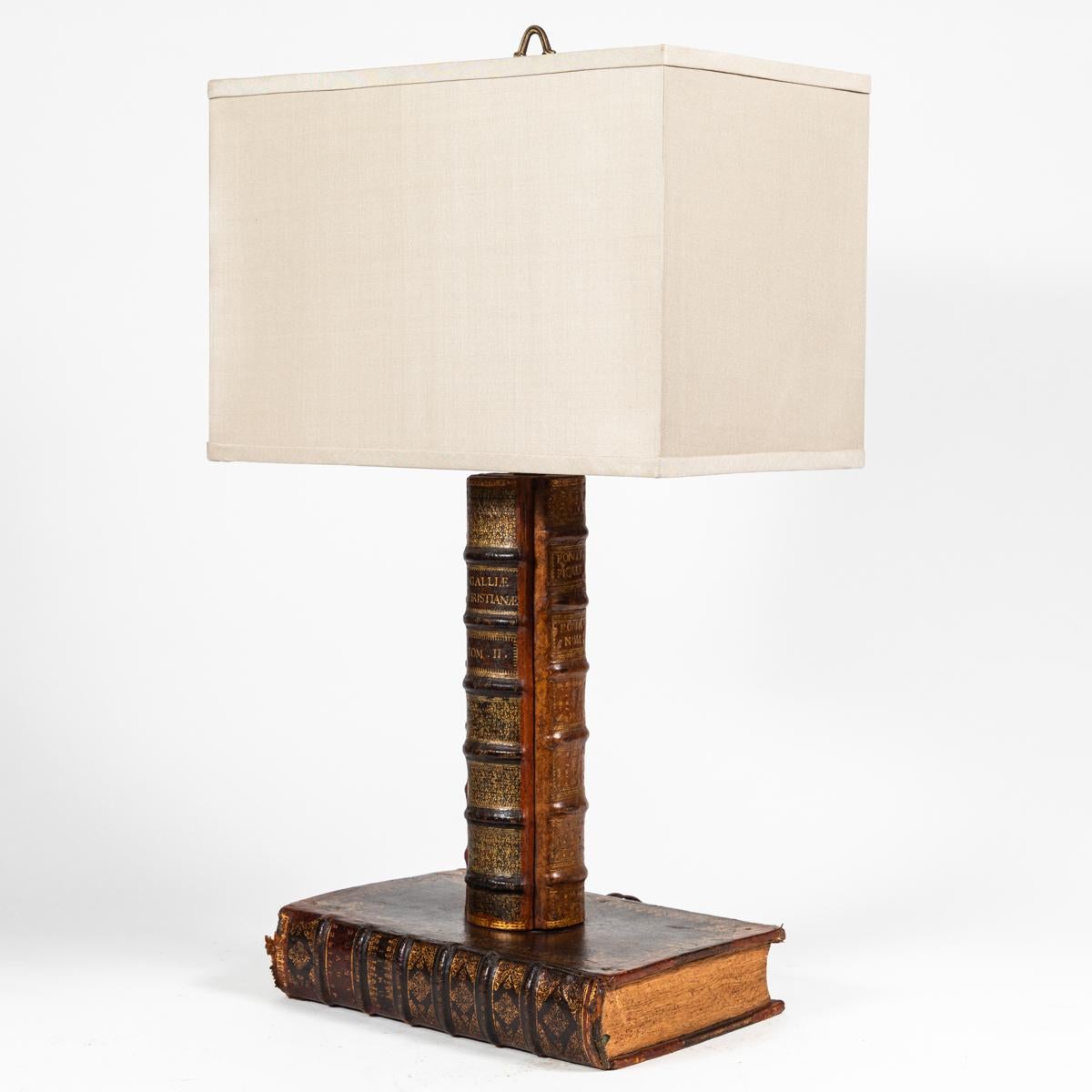 Turn-of-the-century English table lamp with unique, leather-bound book shaped base and support. A handsome yet whimsical piece, the lamp is crowned with a custom, rectangular cream-colored linen shade. Would make a perfect addition to any library or