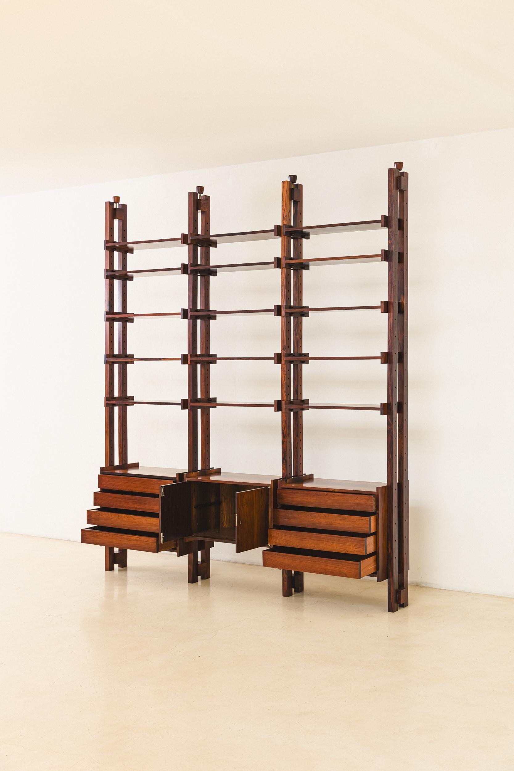 Produced in the 1960s by Celina Decorações, this Rosewood bookshelf has a robust and elaborate structure. Built with four columns, two drawer modules, and one cabinet module, it can accommodate up to fifteen shelves. Each column is made of two large