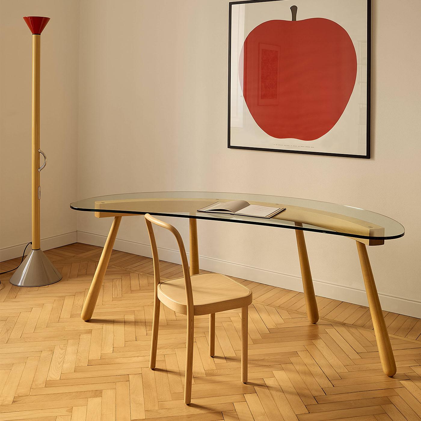 The boomerang curved transparent glass desk, designed by Enzo Mari, features a distinctive curved laminated beam inspired by architectural boomerang shapes and supported by four slender solid legs. Its extralight tempered glass top mirrors the