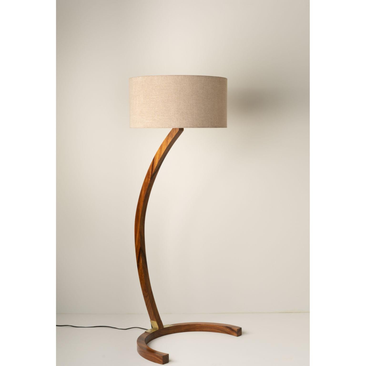 Boomerang Floor Lamp by Isabel Moncada
Dimensions: Ø 76 x H 170 cm.
Materials: Natural matte parota wood, hand-forged brushed brass, fiberglass and linen.

Formed by two arches, this stylized floor luminaire is a statement piece that bears
