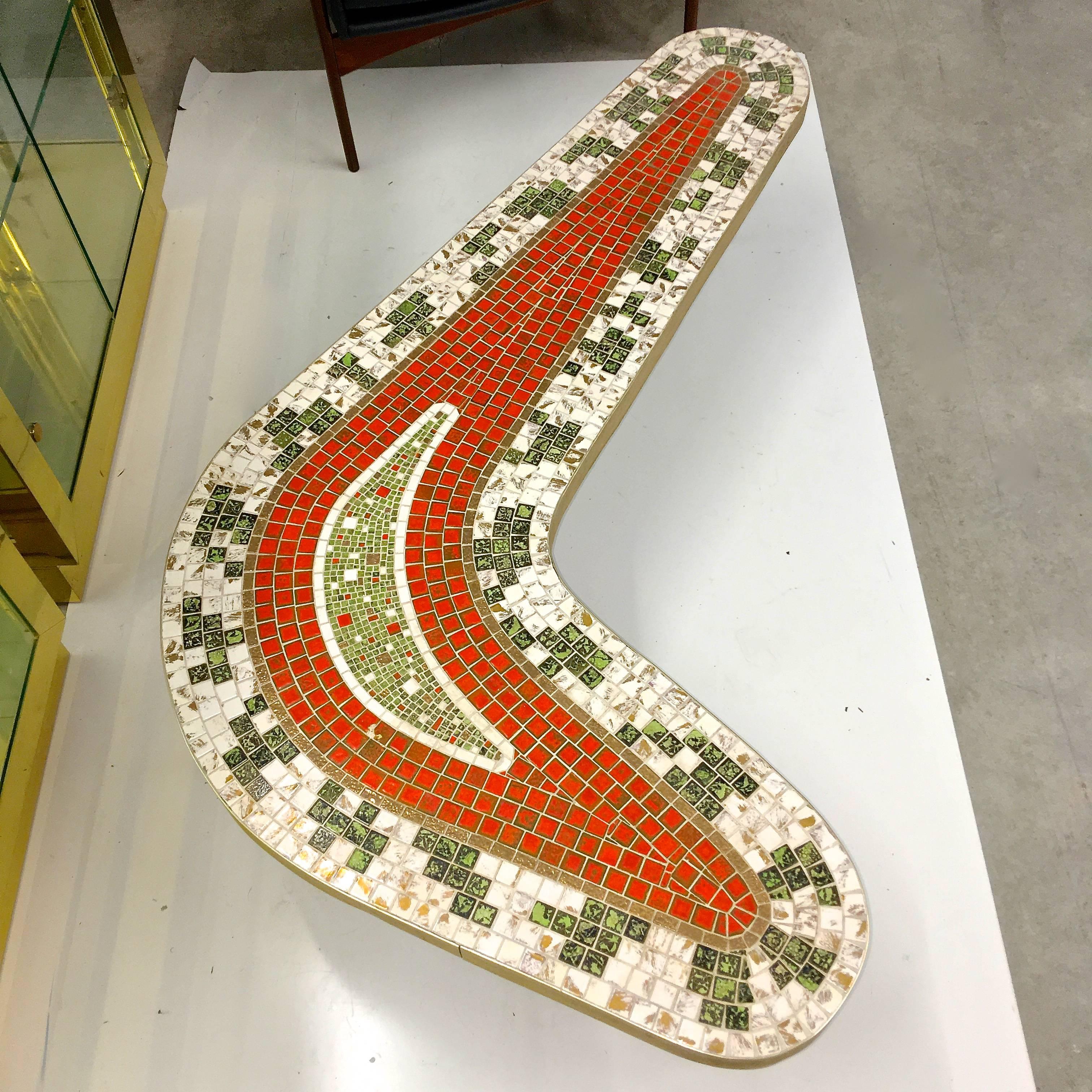 Late 1950s Mid-Century Modern biomorphic-form cocktail table with abstract design in glazed mosaic tiles, brass-tone metal edge banding and three tapered brass finished metal legs.

Colors of the tiles are tones of green, orange, gold and