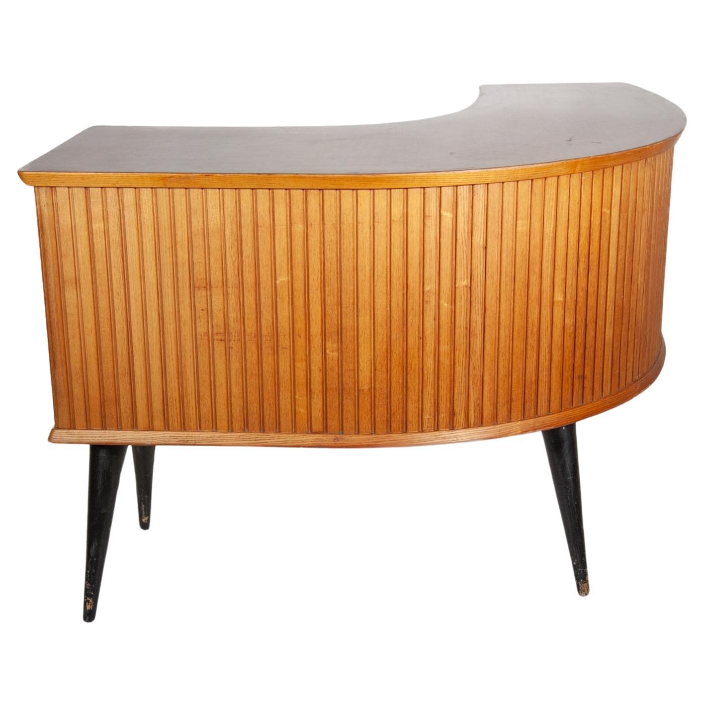 Custom made handcrafted shop counter or desk in a boomerang line with vertical slats at the front which emphasizes the curve of the arch even more, on the inside one side with 3 sliders and metal grip at the other side one door with grip in the