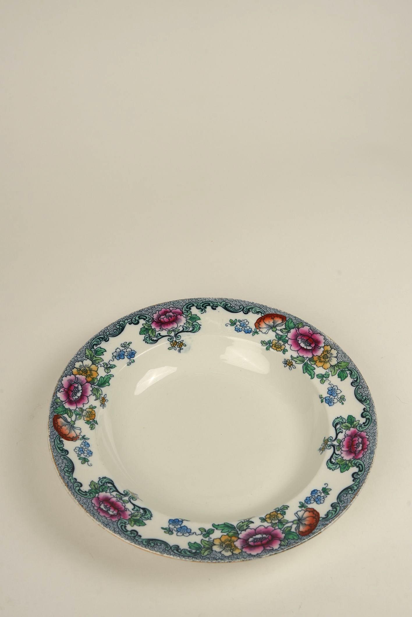 This vibrant floral bowl is a striking example of early 20th-century English transferware at its finest. What sets the 'Nankin' pattern apart is its exuberant border of hand-tinted blooms in vivid pinks, yellows, and cornflower blues, offset by